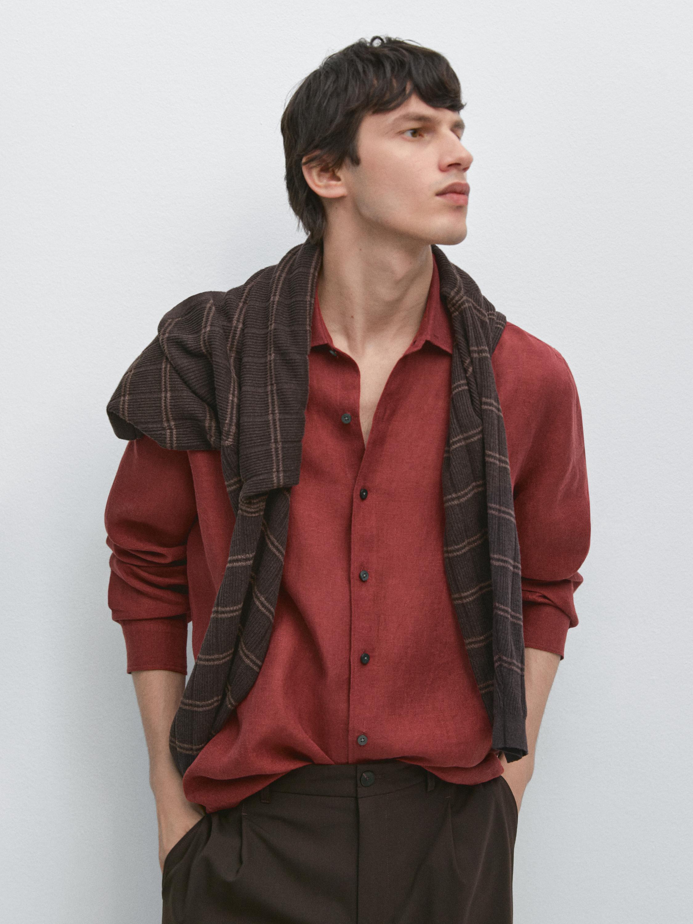 plaintext Plano médio de camisa vermelha com botões pretos e calças castanhas. Camisola castanha com riscas sobre os ombros.