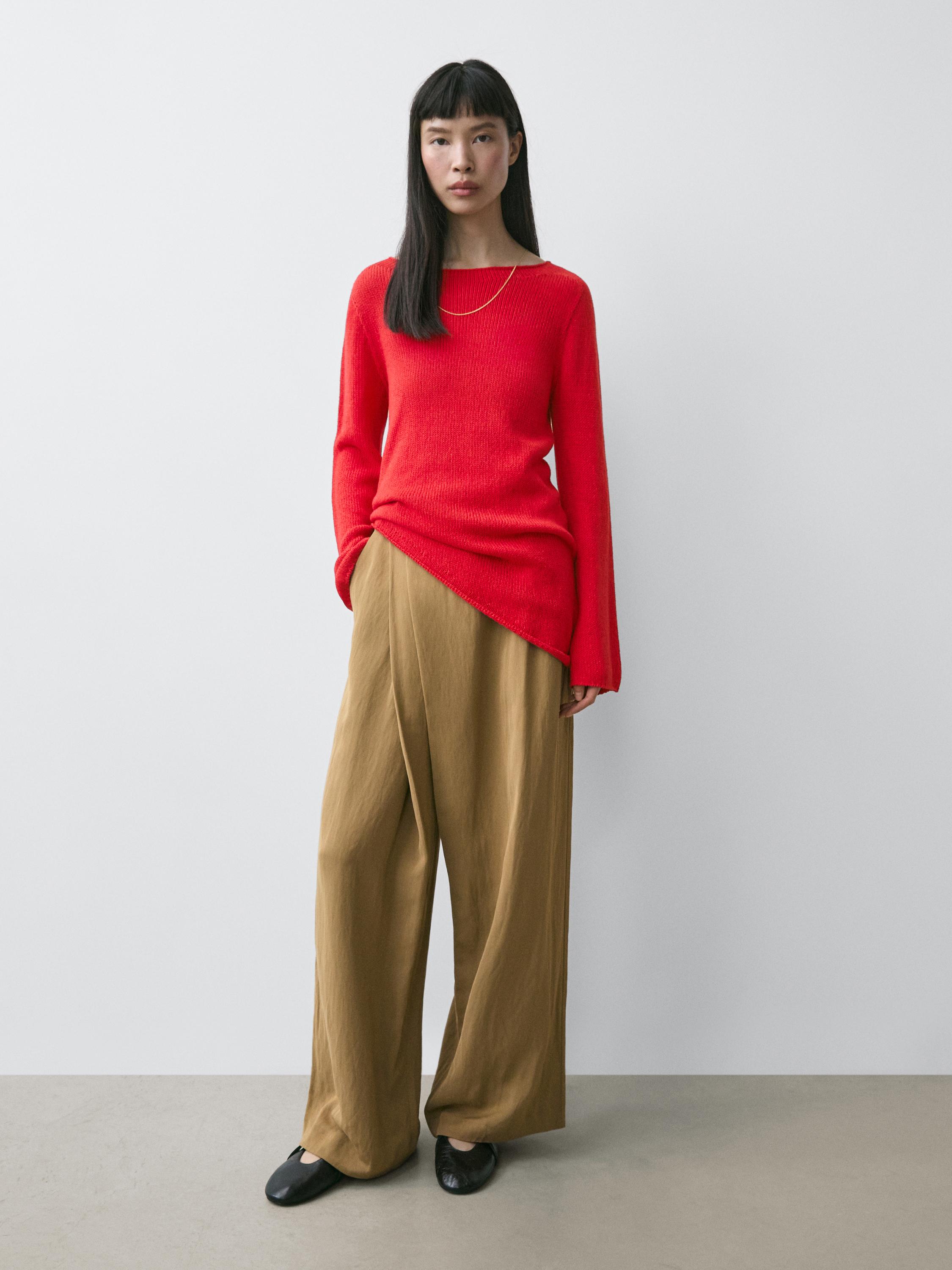 Комплет од црвен џемпер со асиметричен крој и широки кафеави панталони.