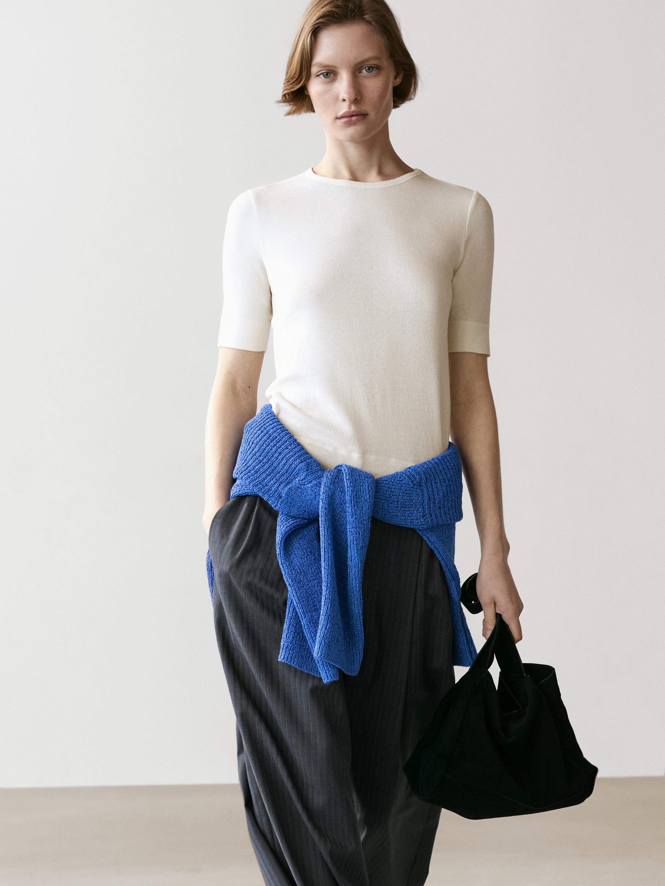 Ensemble composé d'un T-shirt écru à manches courtes, d'un pantalon foncé à rayures et d'un pull bleu noué à la taille.