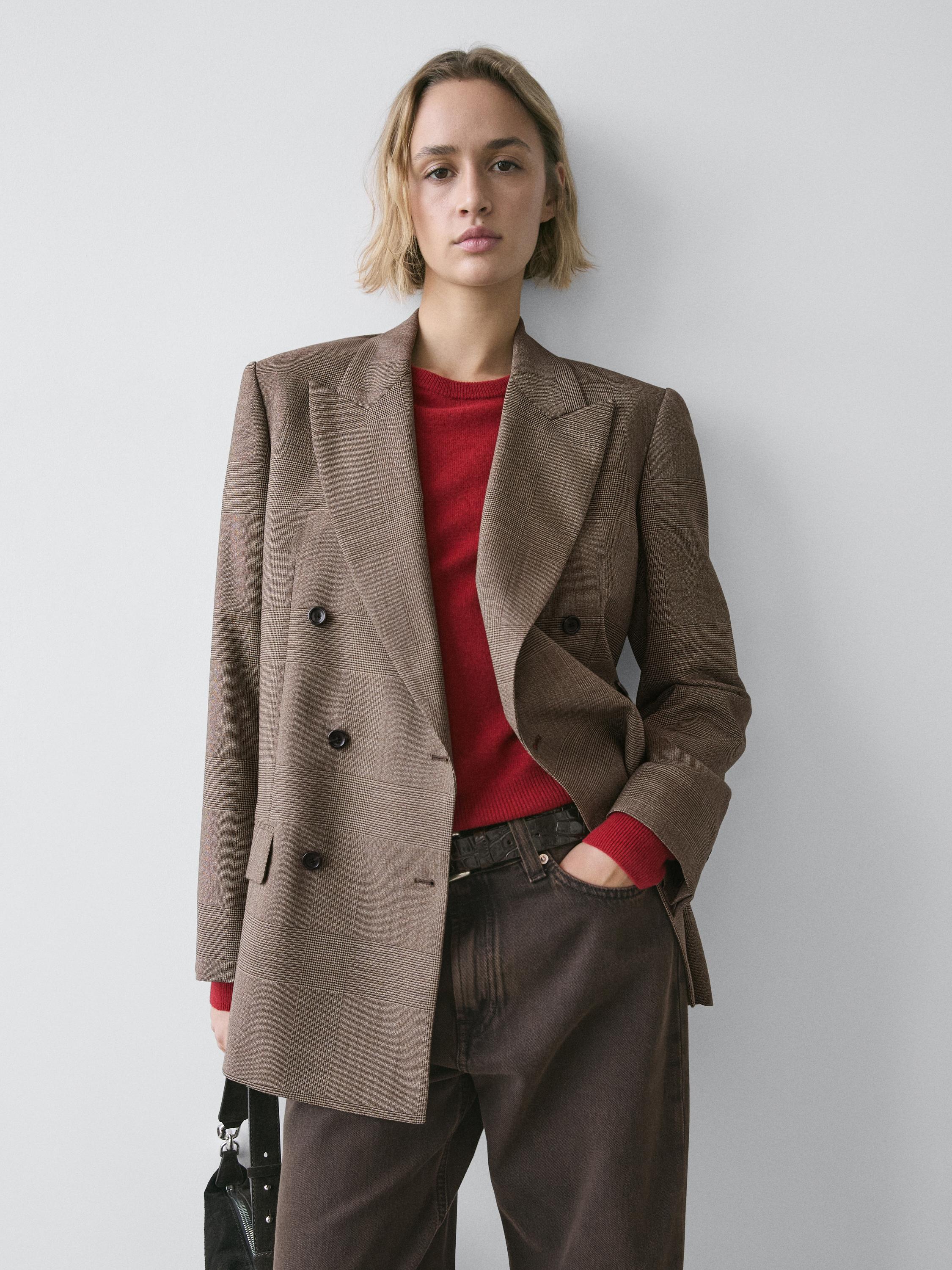 طقم بليزر بيج مزدوج الصدر بأزرار سوداء، سويتر أحمر وبنطلون بني.