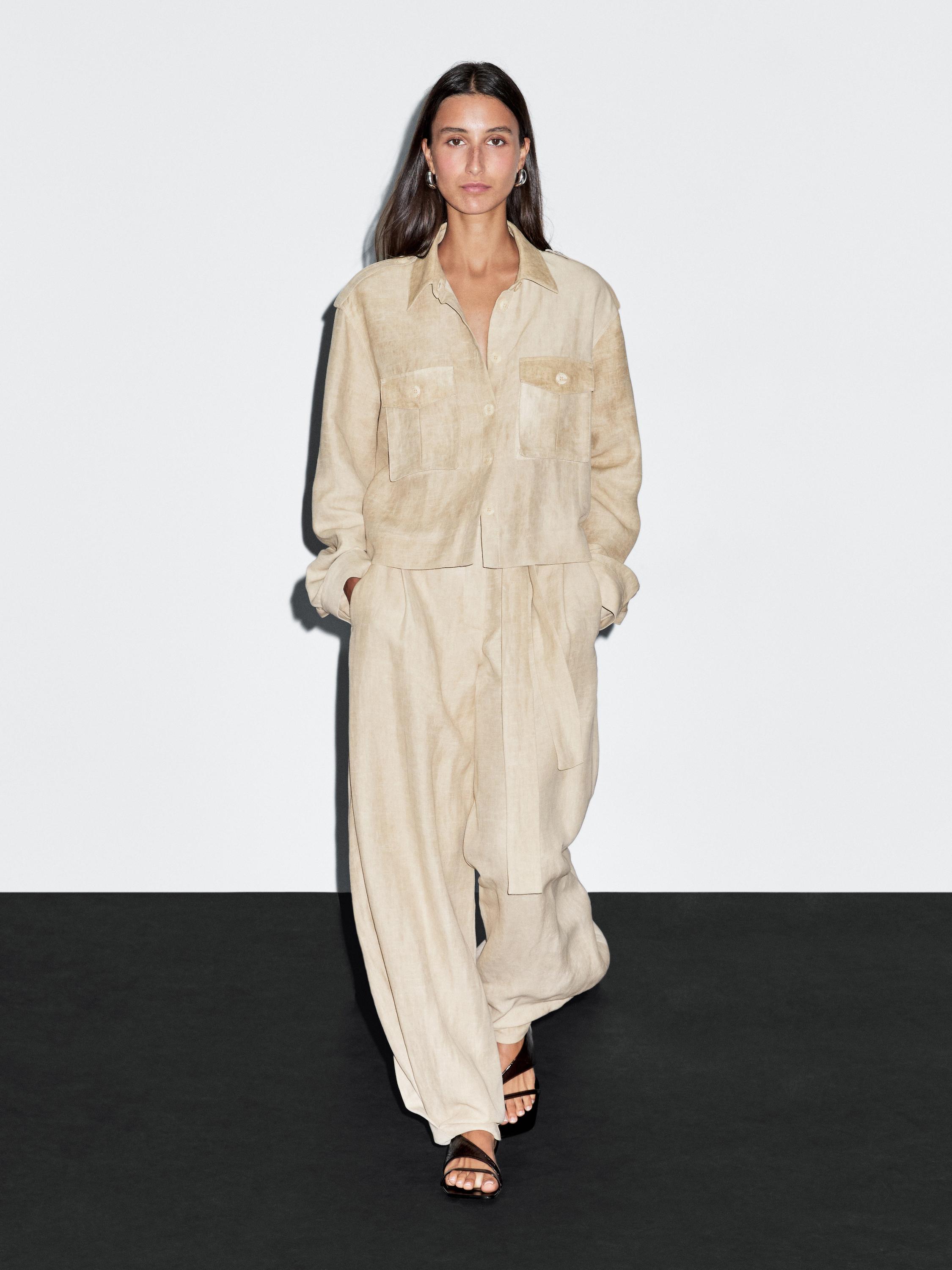 Ensemble composé d'une chemise couleur sable avec poches frontales et d'un pantalon large assorti avec ceinture, le tout combiné avec des sandales noires.