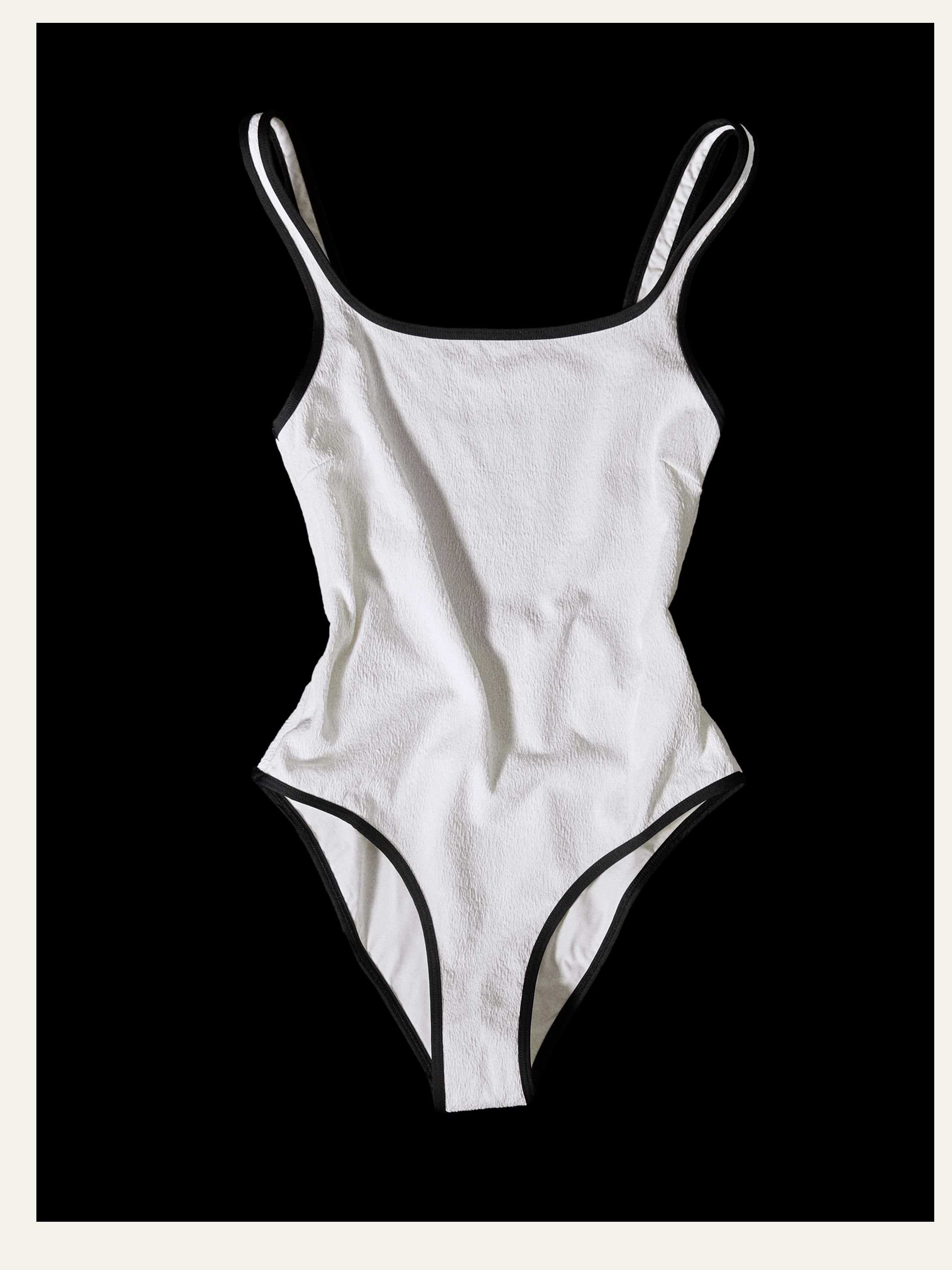 Vista frontal de bañador blanco roto con textura y ribetes negros, tirantes finos y corte alto en las piernas.