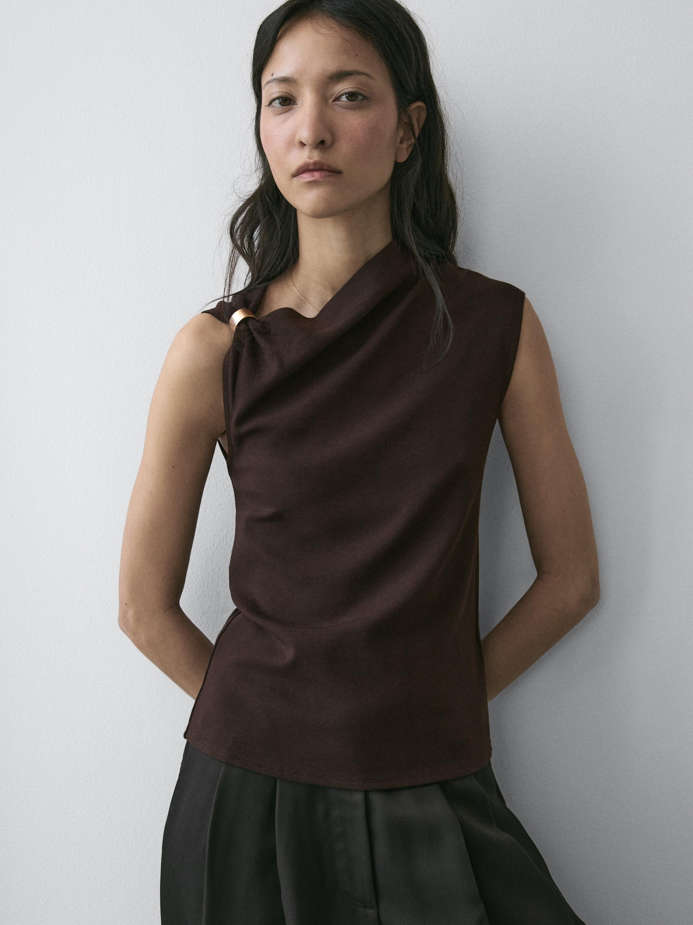 Asymmetrical sleeveless brown top set with a brooch detail on the shoulder.