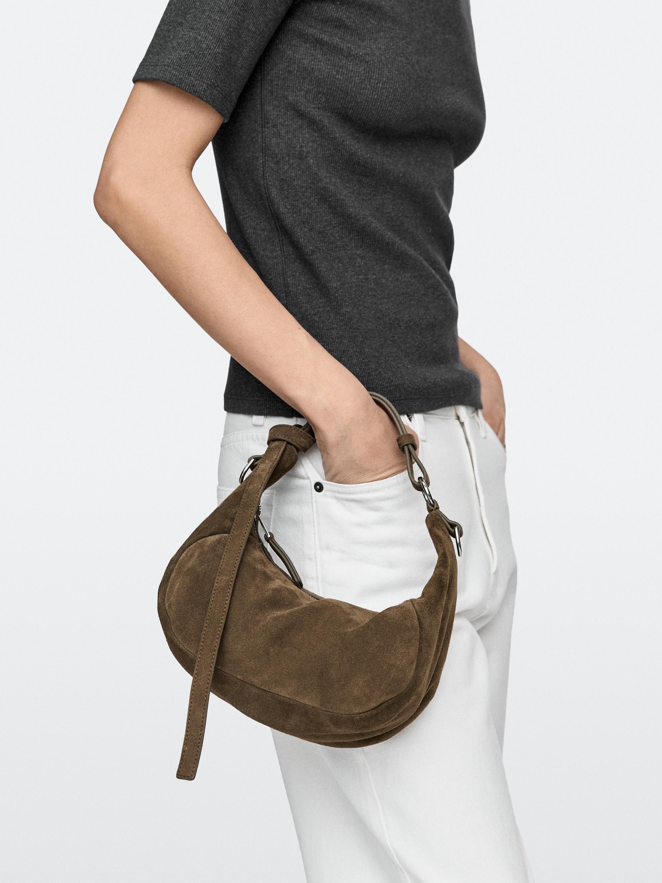 Afbeelding van een kaki handtas met kort hengsel en ritssluiting, vastgehouden in de hand.