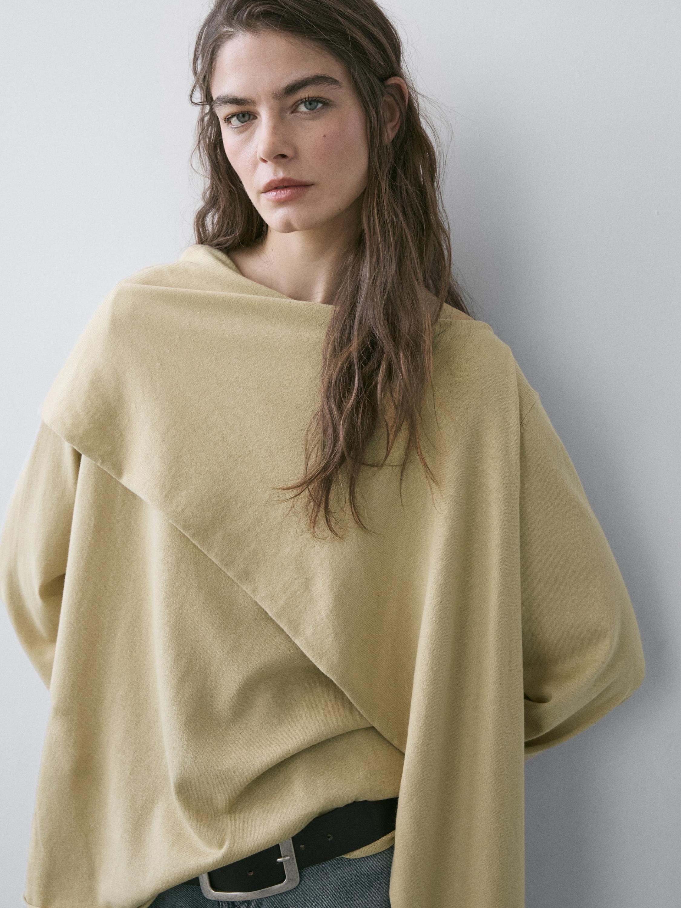 Plano medio de jersey verdoso con detalle de pañuelo cruzado en el pecho.