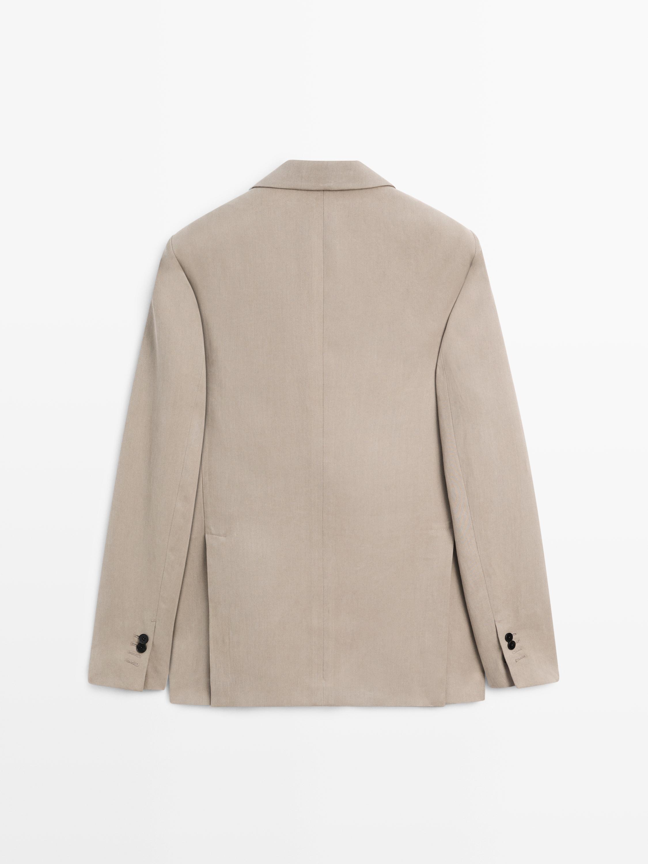 Vista posterior de blazer beis con solapas clásicas e petos laterais. Detalle de botóns negros nos puños.