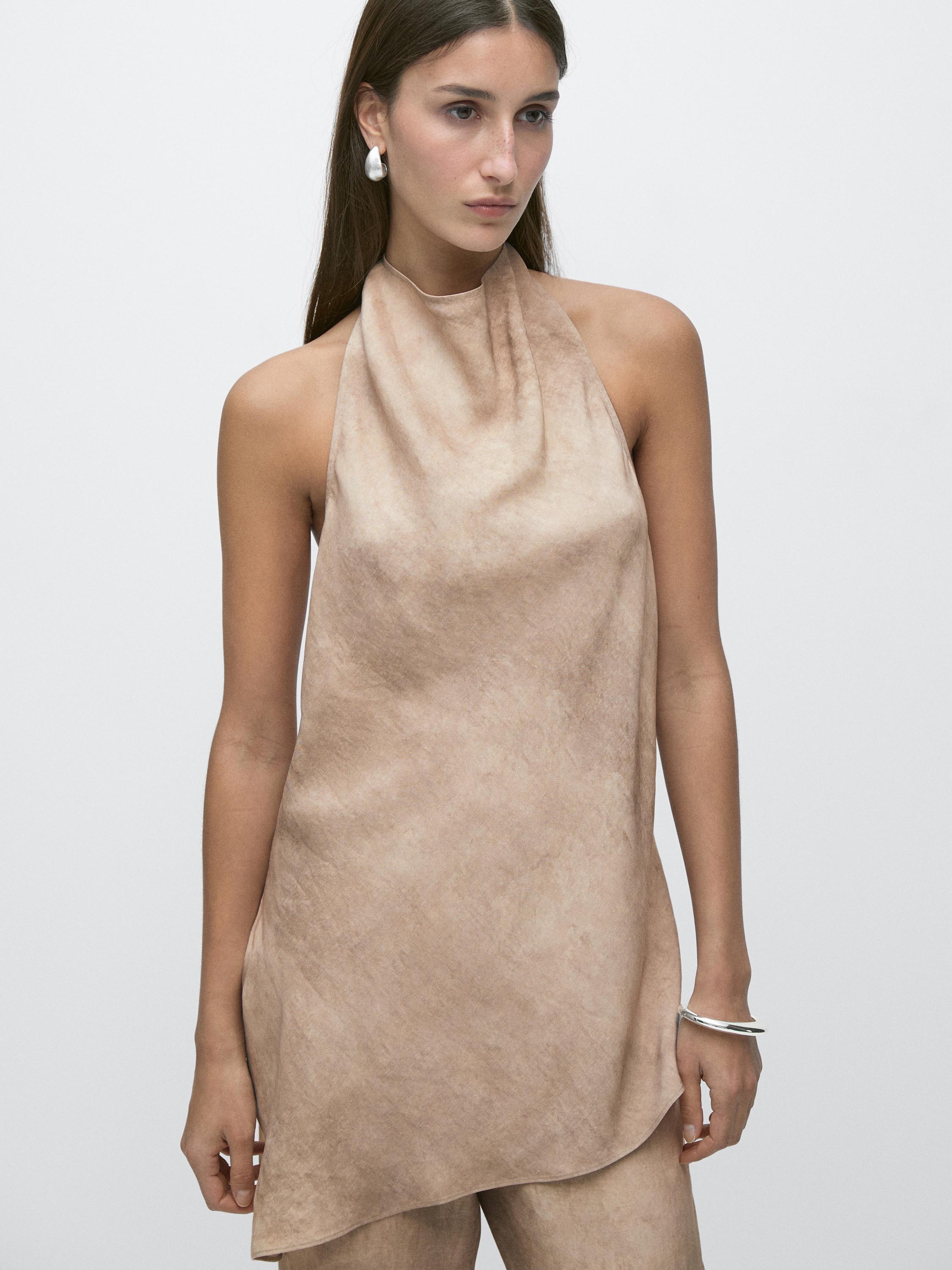 Plano medio de top color piedra sin mangas con cuello halter y corte asimétrico.