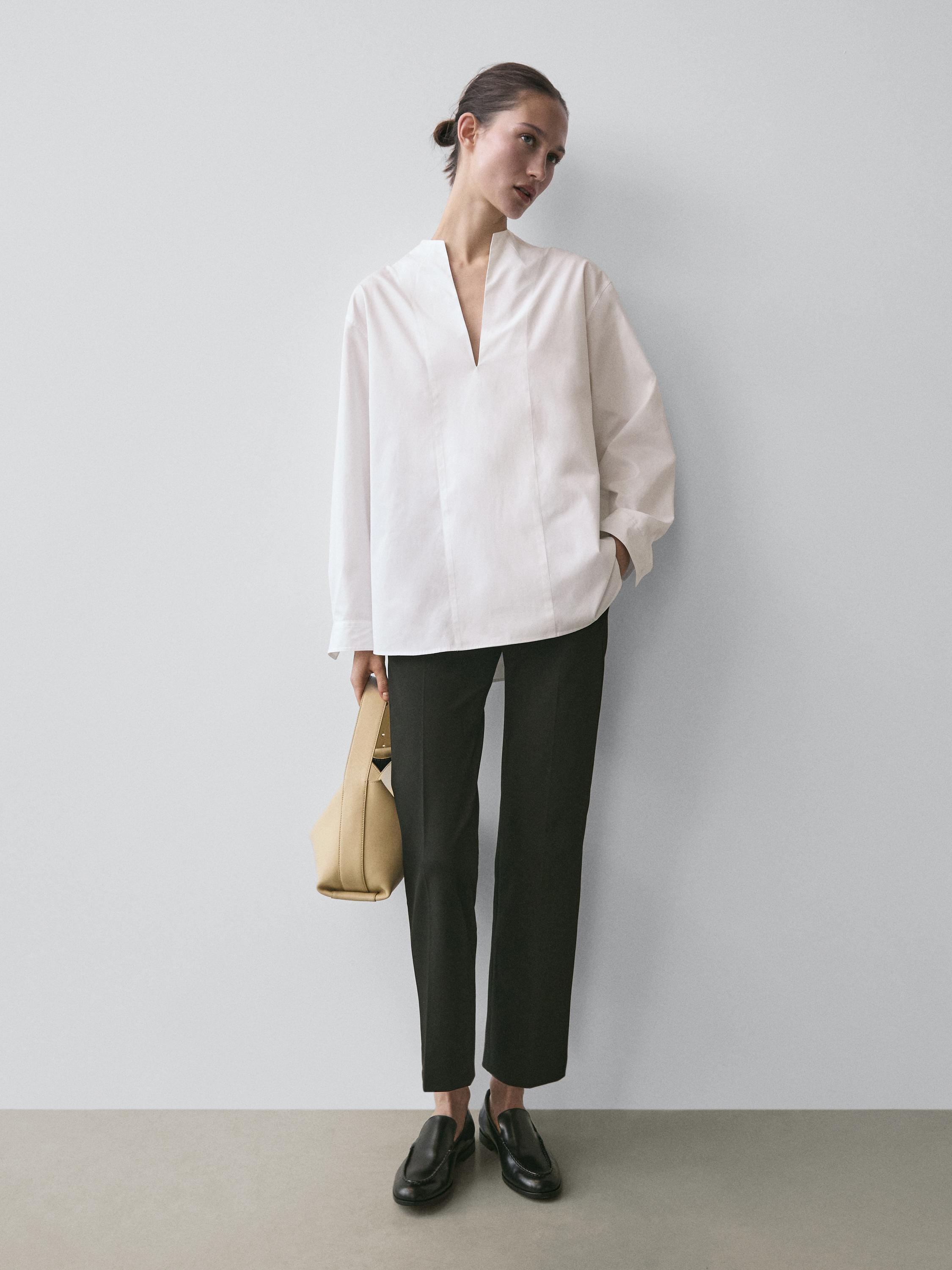 Komplet me këmishë të bardhë me jakë të hapur dhe pantallona të zeza të drejta.