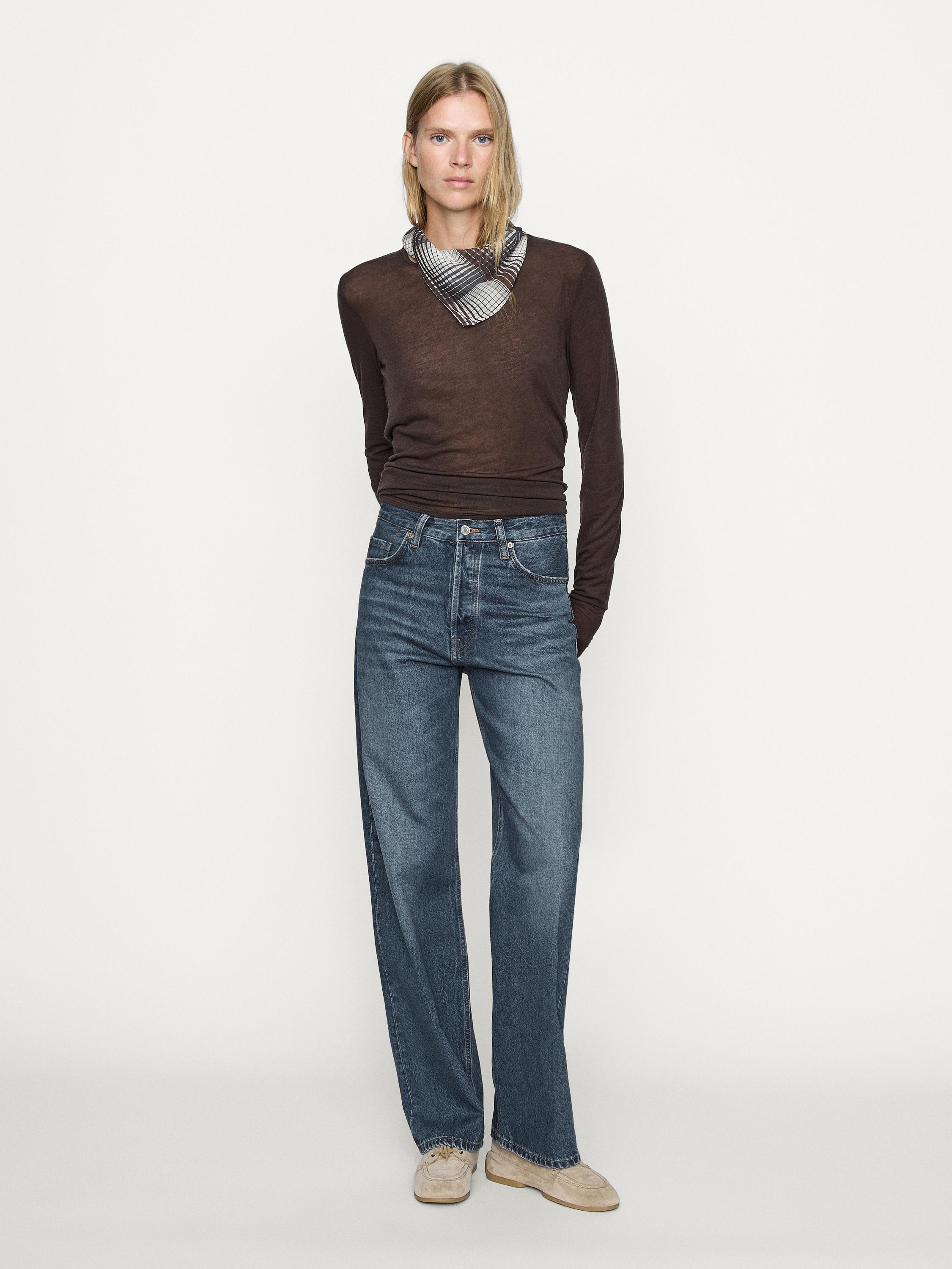 Completo di jeans blu medio straight fit a vita alta e maglione marrone a maniche lunghe con foulard a quadri al collo.