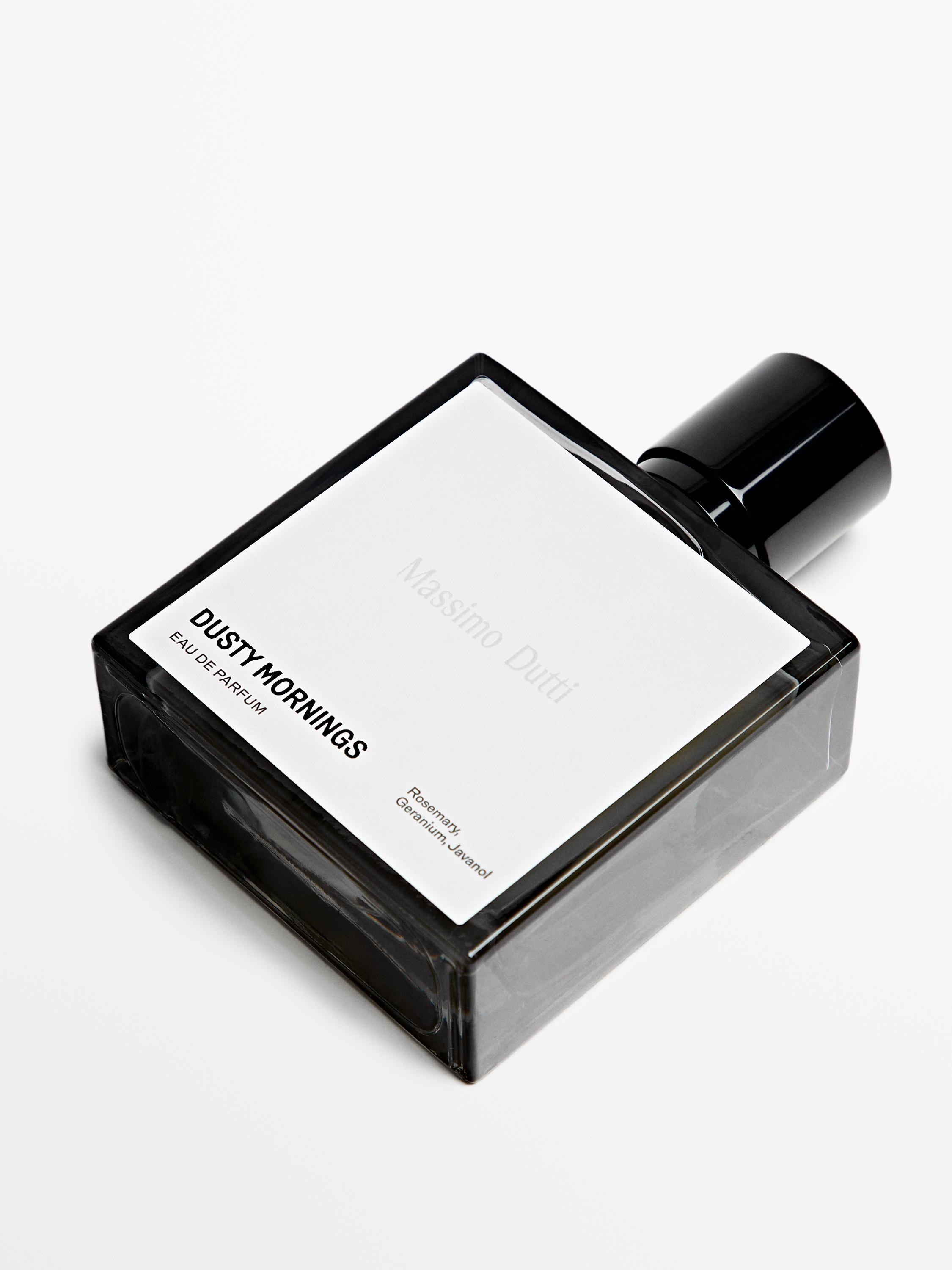 Botella de perfume gris perla con texto "DUSTY MORNINGS EAU DE PARFUM" y "Romero, Geranio, Hyland" en la etiqueta blanca.