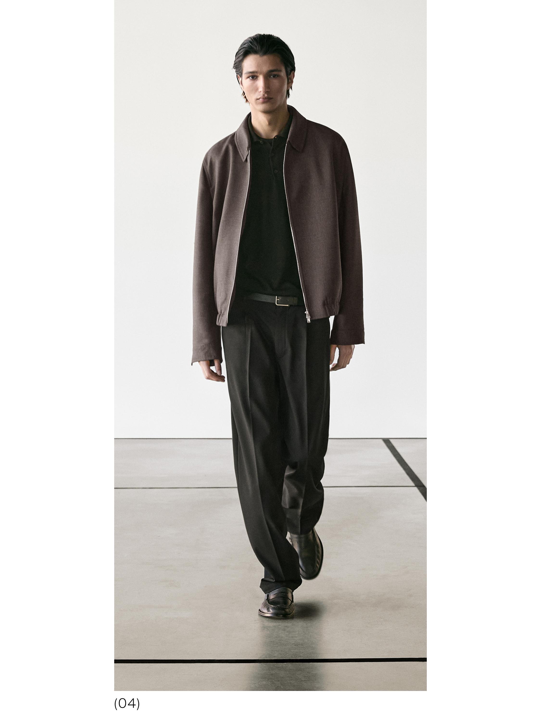 Brūns džemperis ar rāvējslēdzēju, melns polo krekls un melnas taisna piegriezuma bikses.