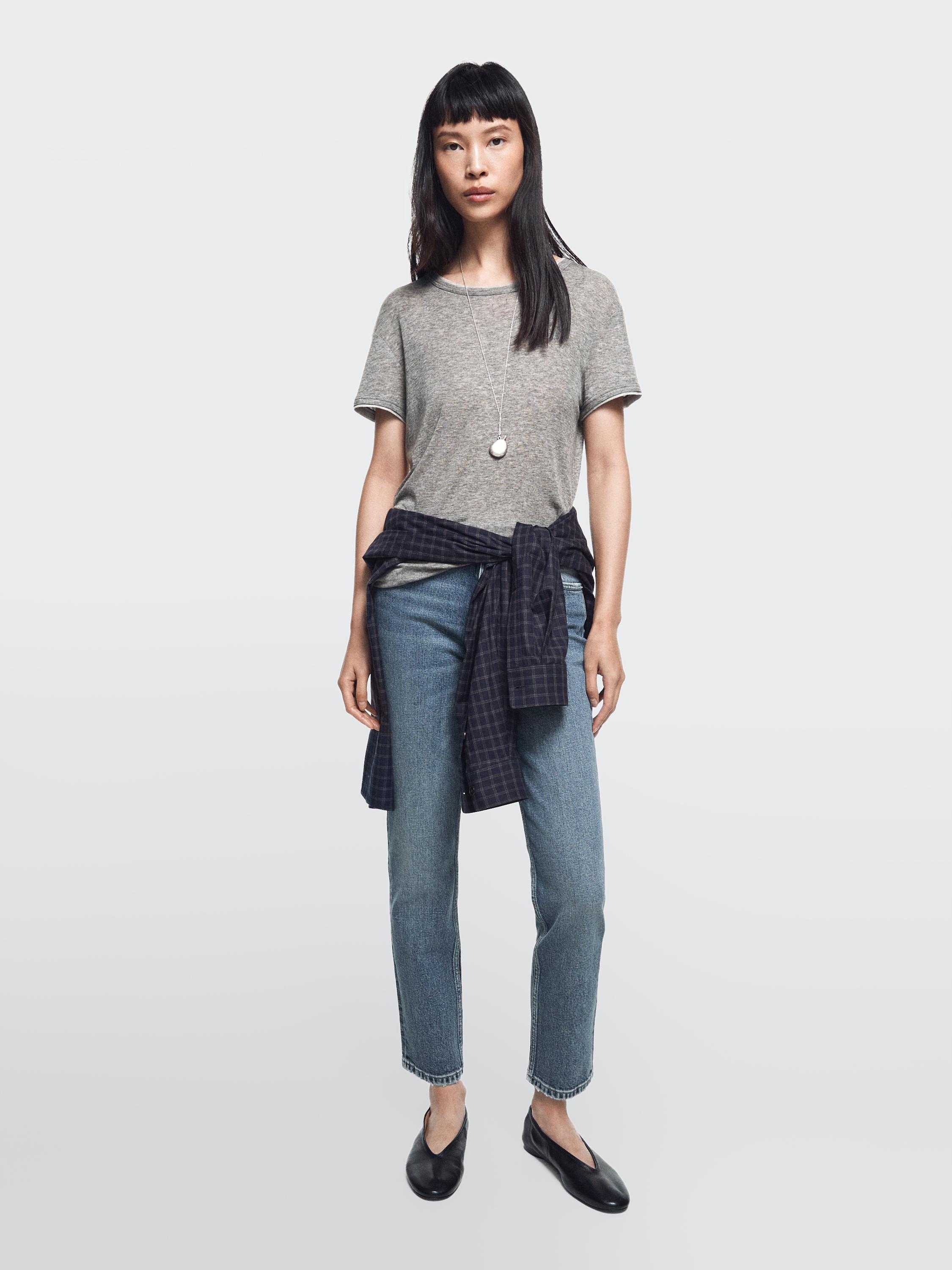 Completo di jeans blu medio slim fit a vita media e t-shirt grigia, con camicia a quadri legata in vita.