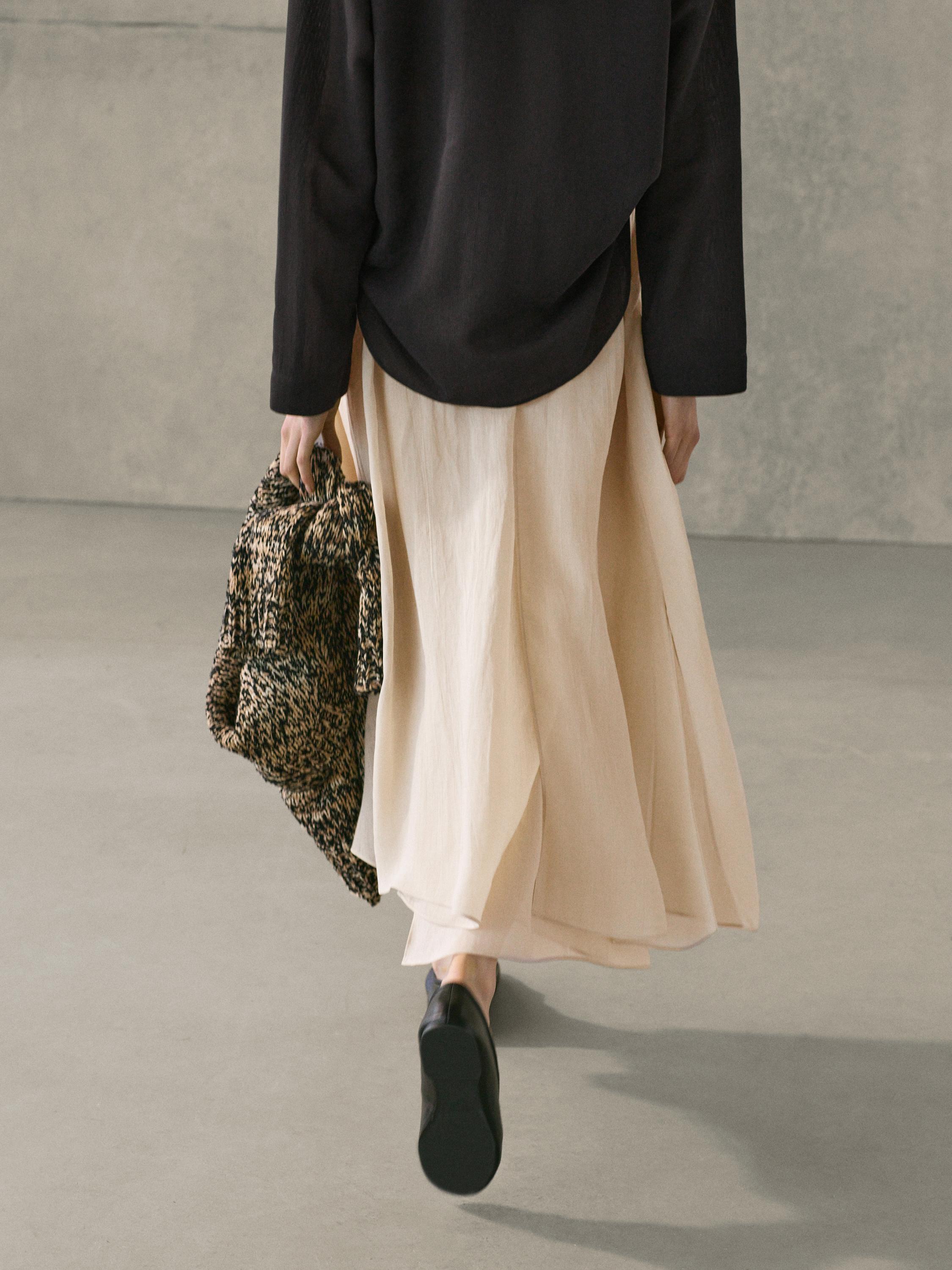 Black blouse and wide ecru culotte skirt set, with a woven bag in hand and black shoes.