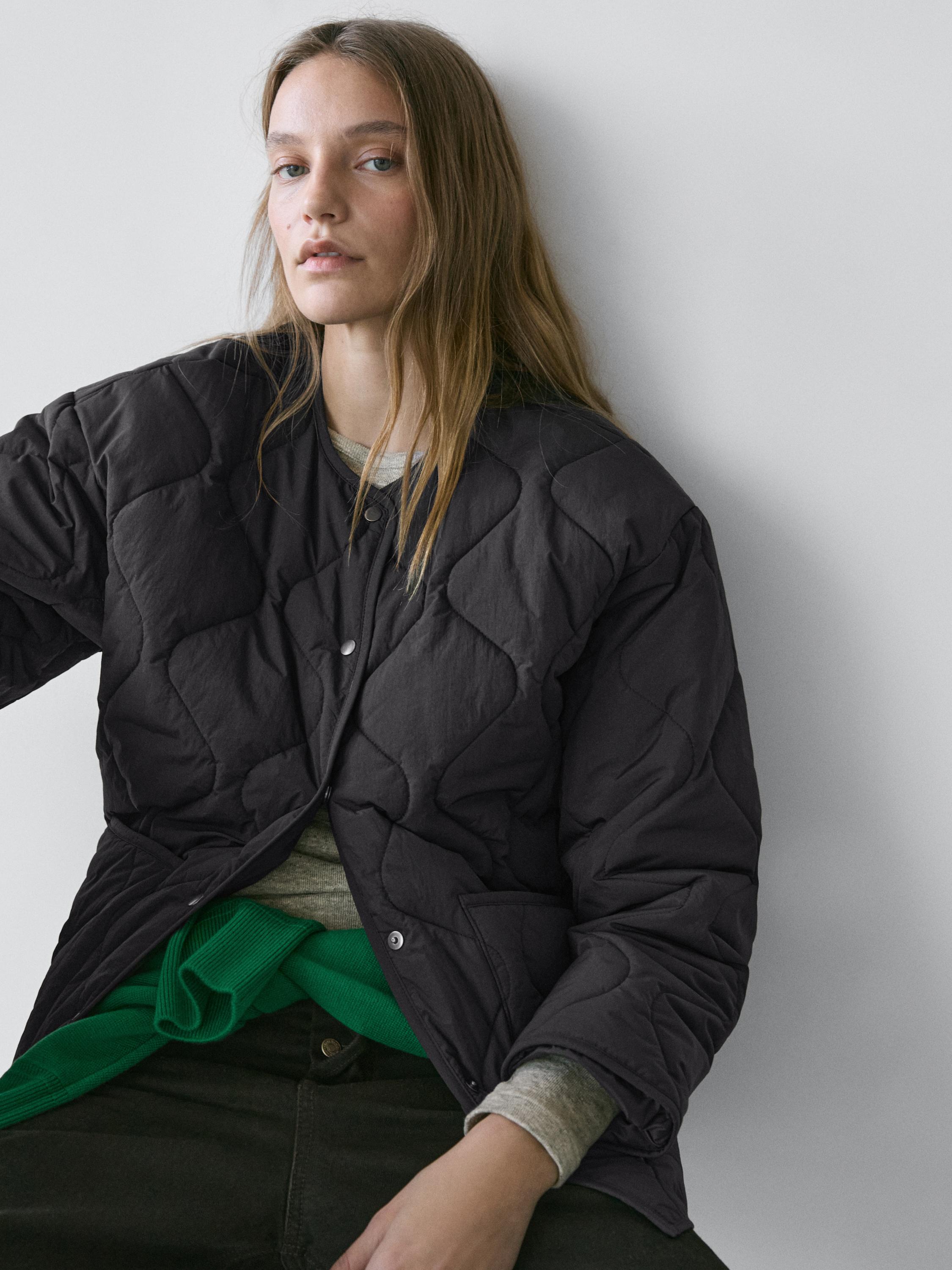 Półzbliżenie czarnej pikowanej kurtki zapinanej na zatrzaski, z kieszeniami bocznymi.