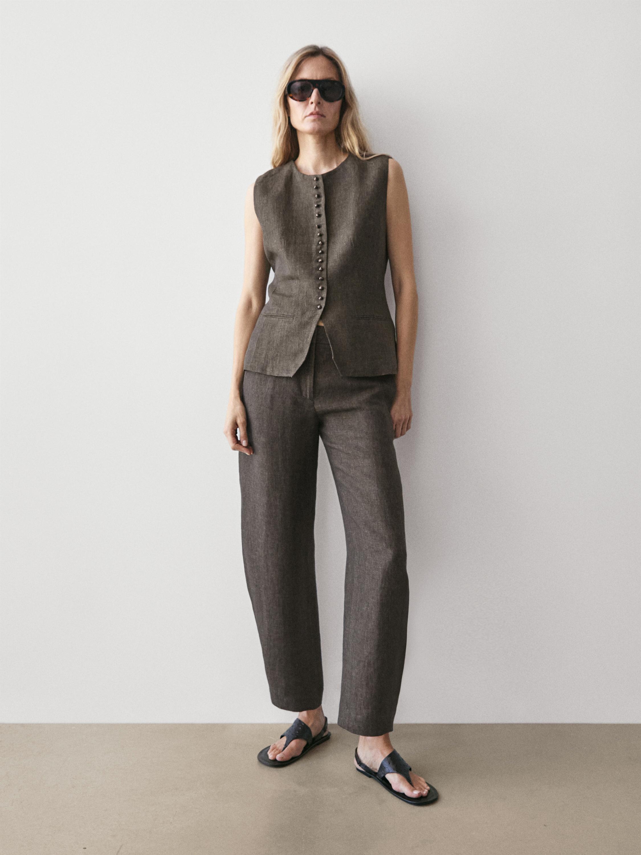 Mouwloos bruin vest met knoopsluiting aan de voorkant en een rechte bruine broek.