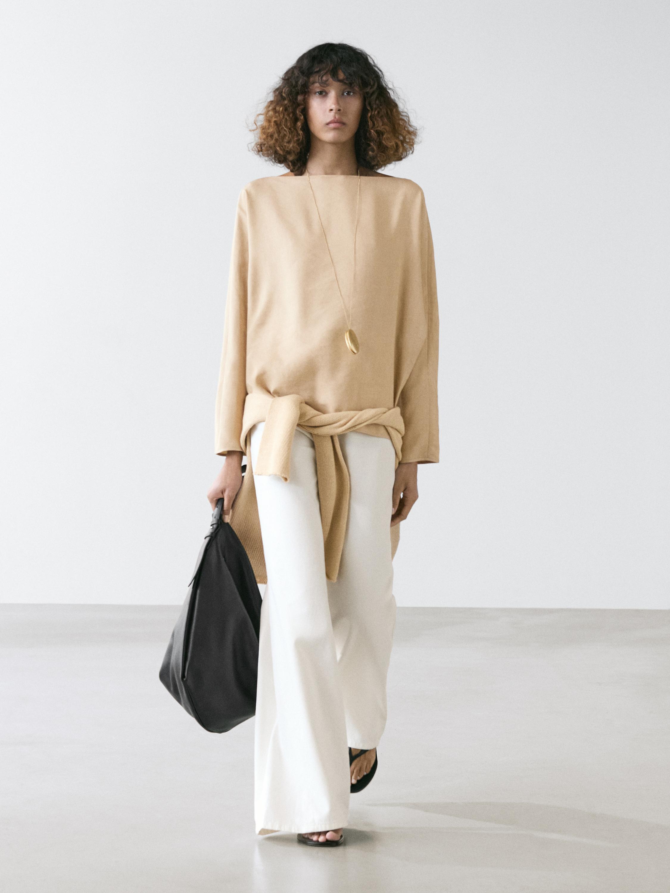 Beige boat neck shirt and white wide-leg pants set. Wears a black bag and sandals.
