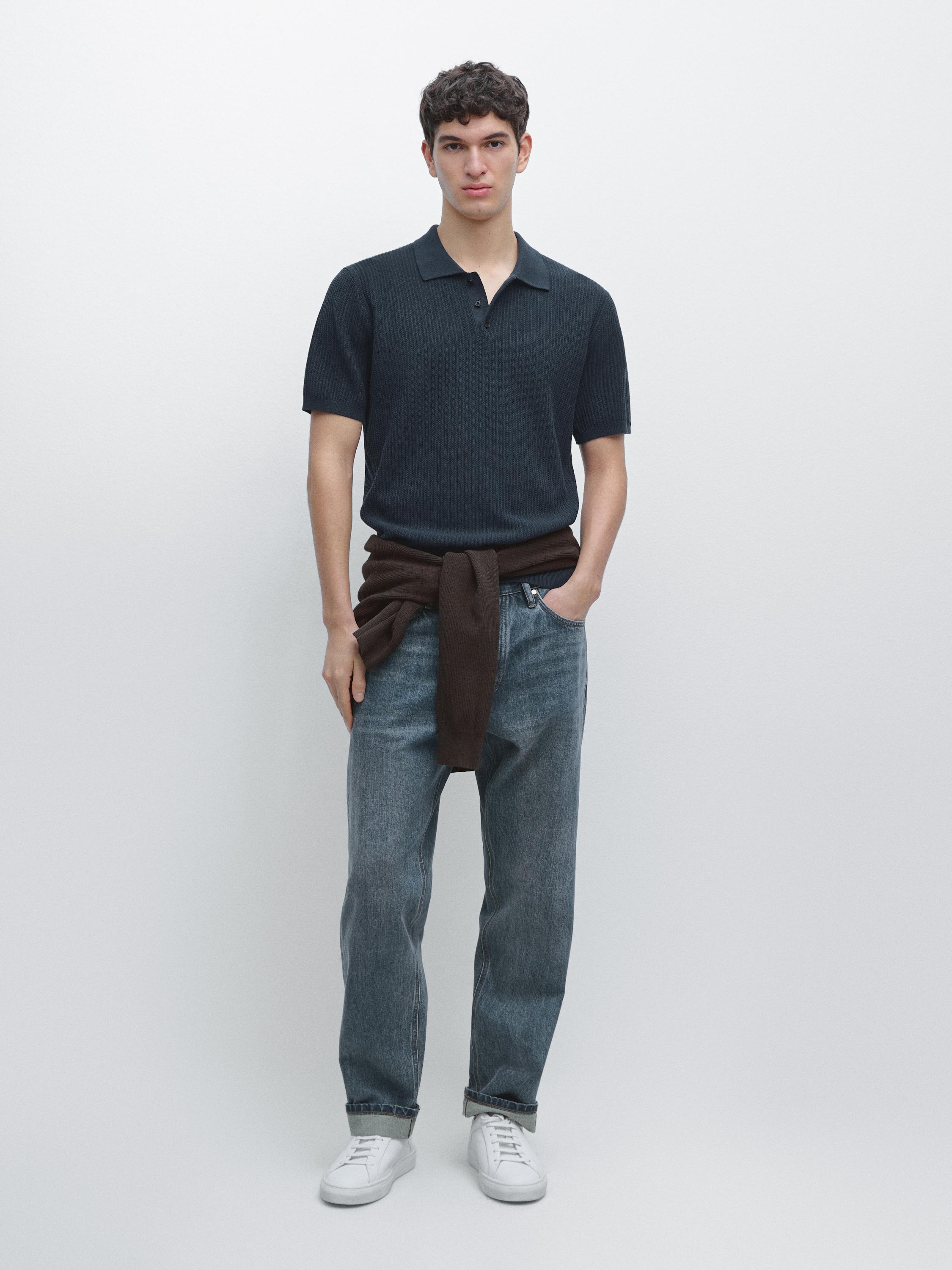 Conjunto de polo azul medio de manga corta, jeans azules y zapatillas blancas. Suéter marrón atado a la cintura.