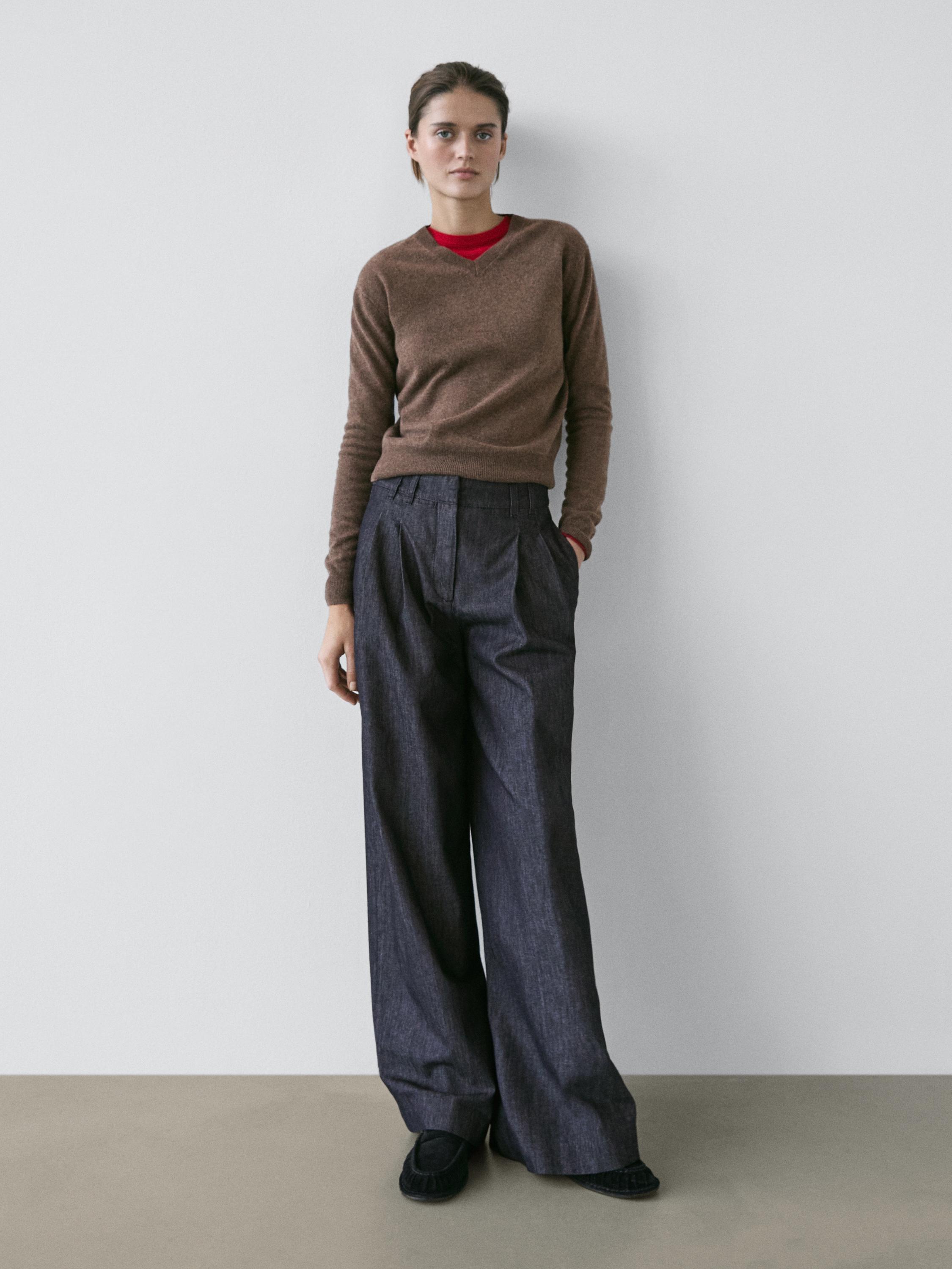 Ensemble composé d'un pull marron, d'un t-shirt rouge et d'un jean bleu foncé taille haute à jambes larges.