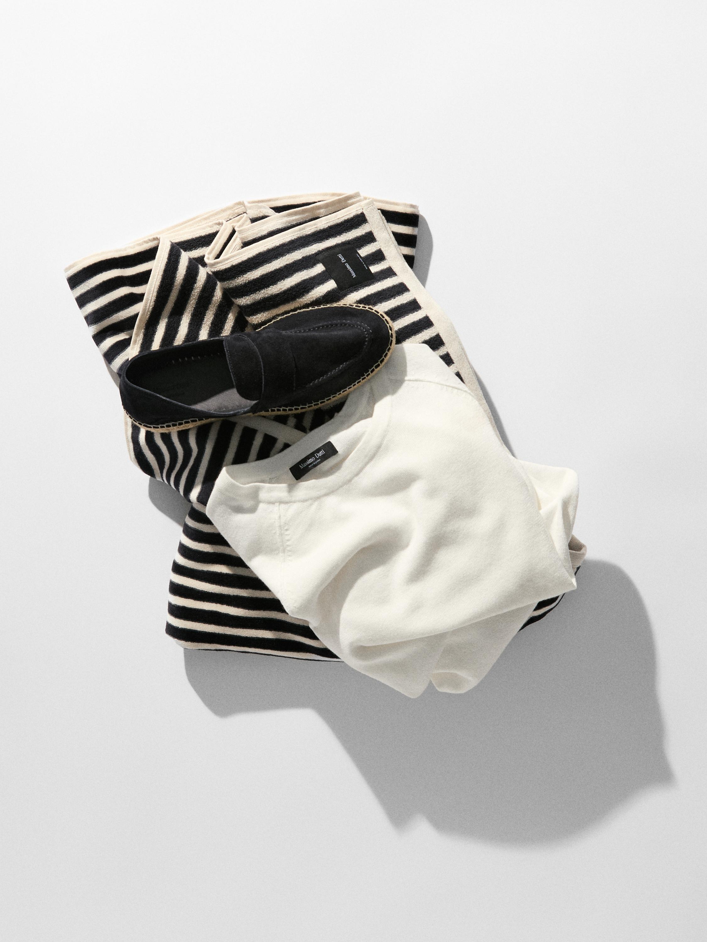 Ensemble composé d'un pull à rayures noires et beiges, d'un t-shirt blanc et de mocassins noirs à surpiqûres visibles.