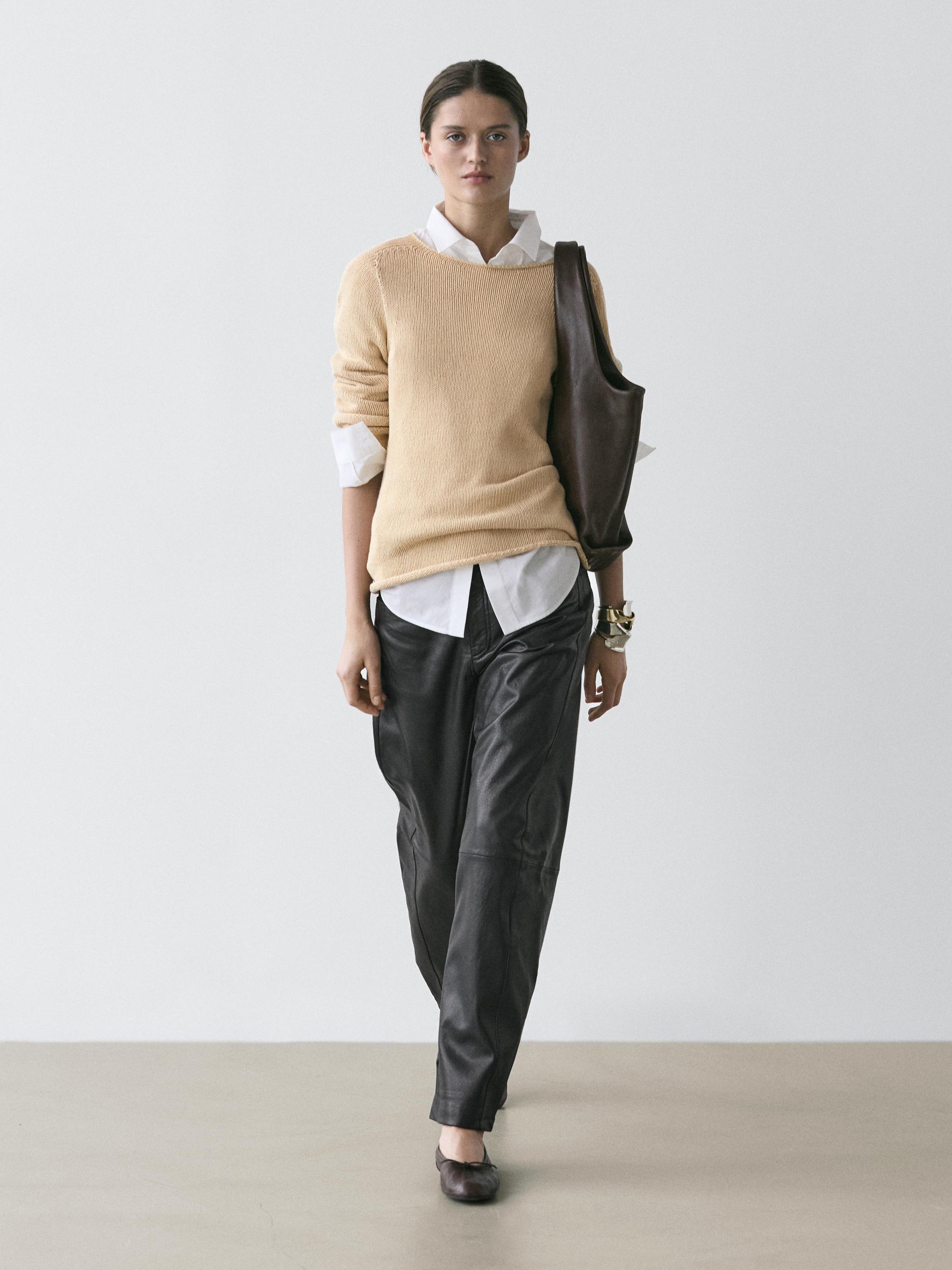 Juodas balloon fit kelnių komplektas ir smėlio spalvos megztinis ant baltų marškinių, rudas rankinukas per petį.