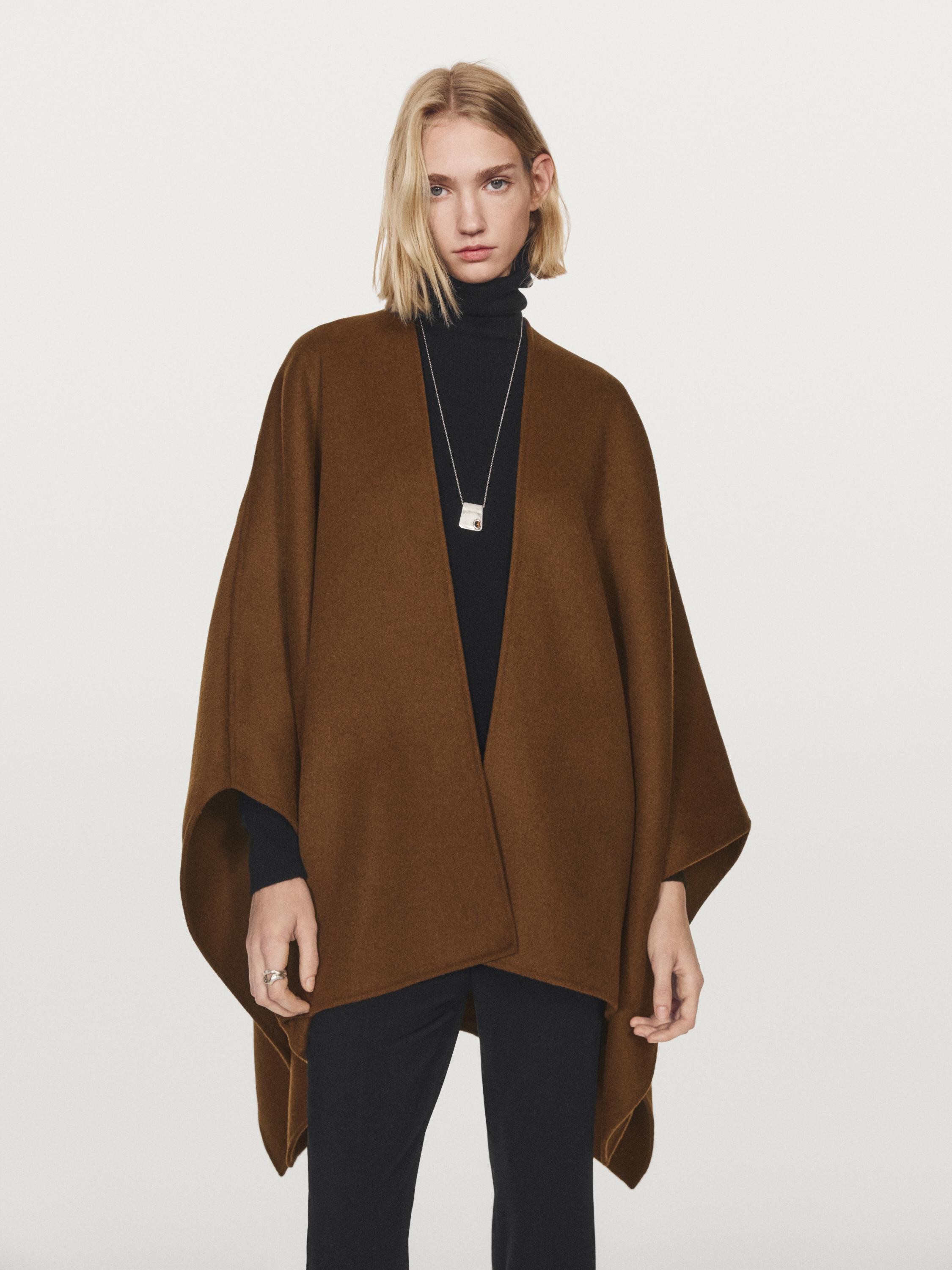 Open camel cape set over a black turtleneck sweater and black pants.