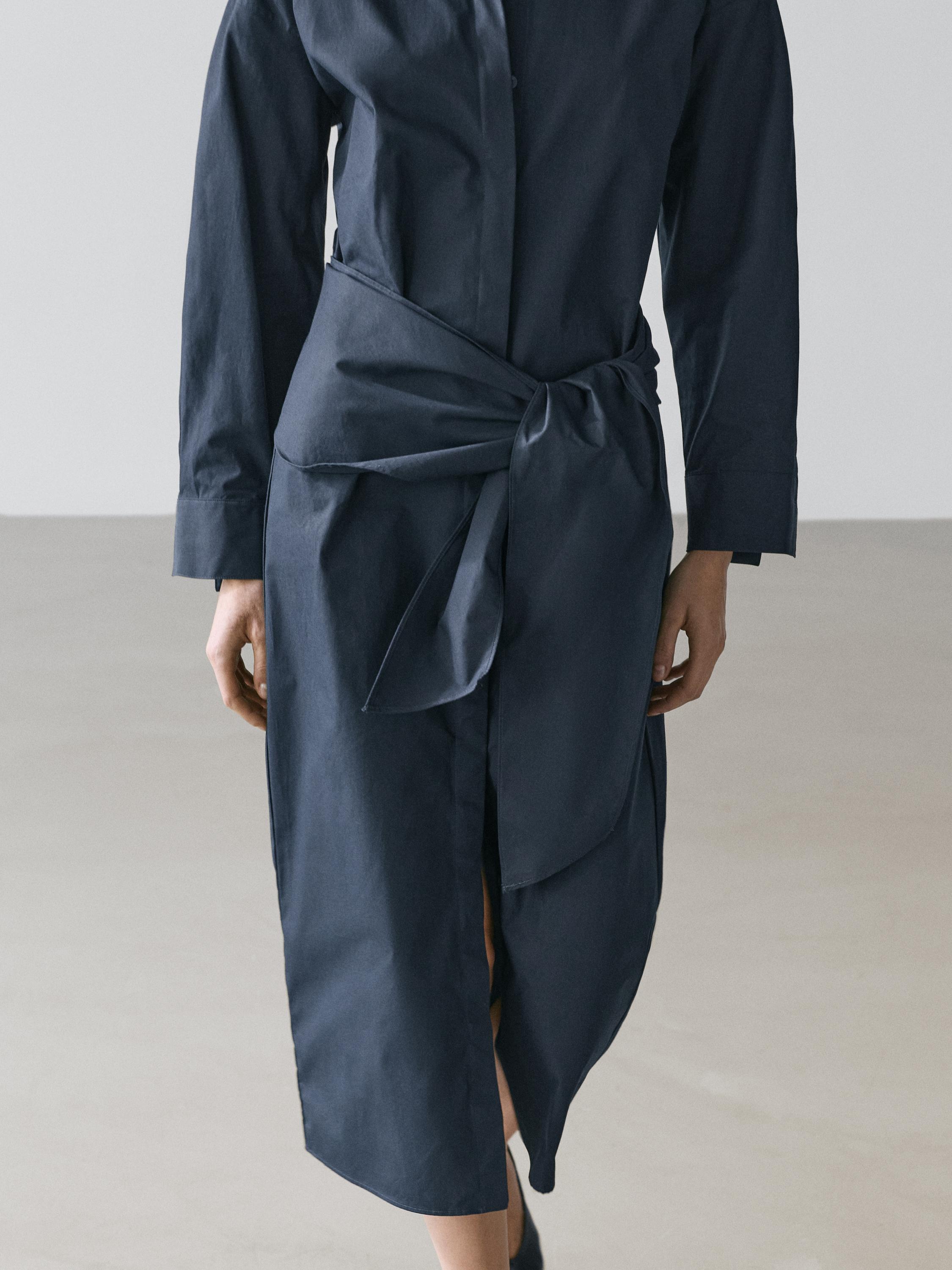 "Plan i mesëm i fustanit këmishë blu me detaj shalli të lidhur në bel dhe çarje para."