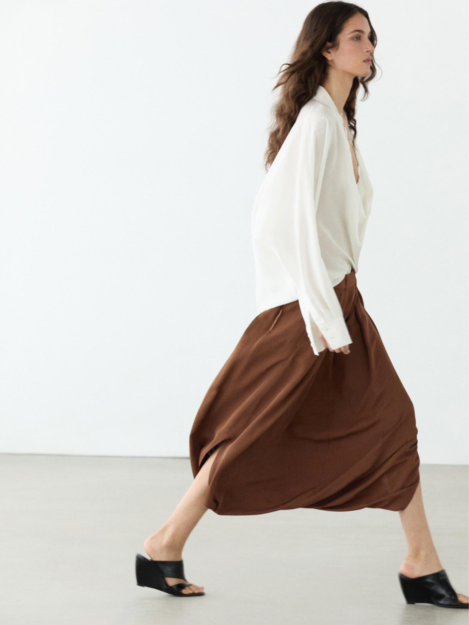 Conjunto de blusa blanca de manga larga y falda pantalón marrón fluida con pliegues.