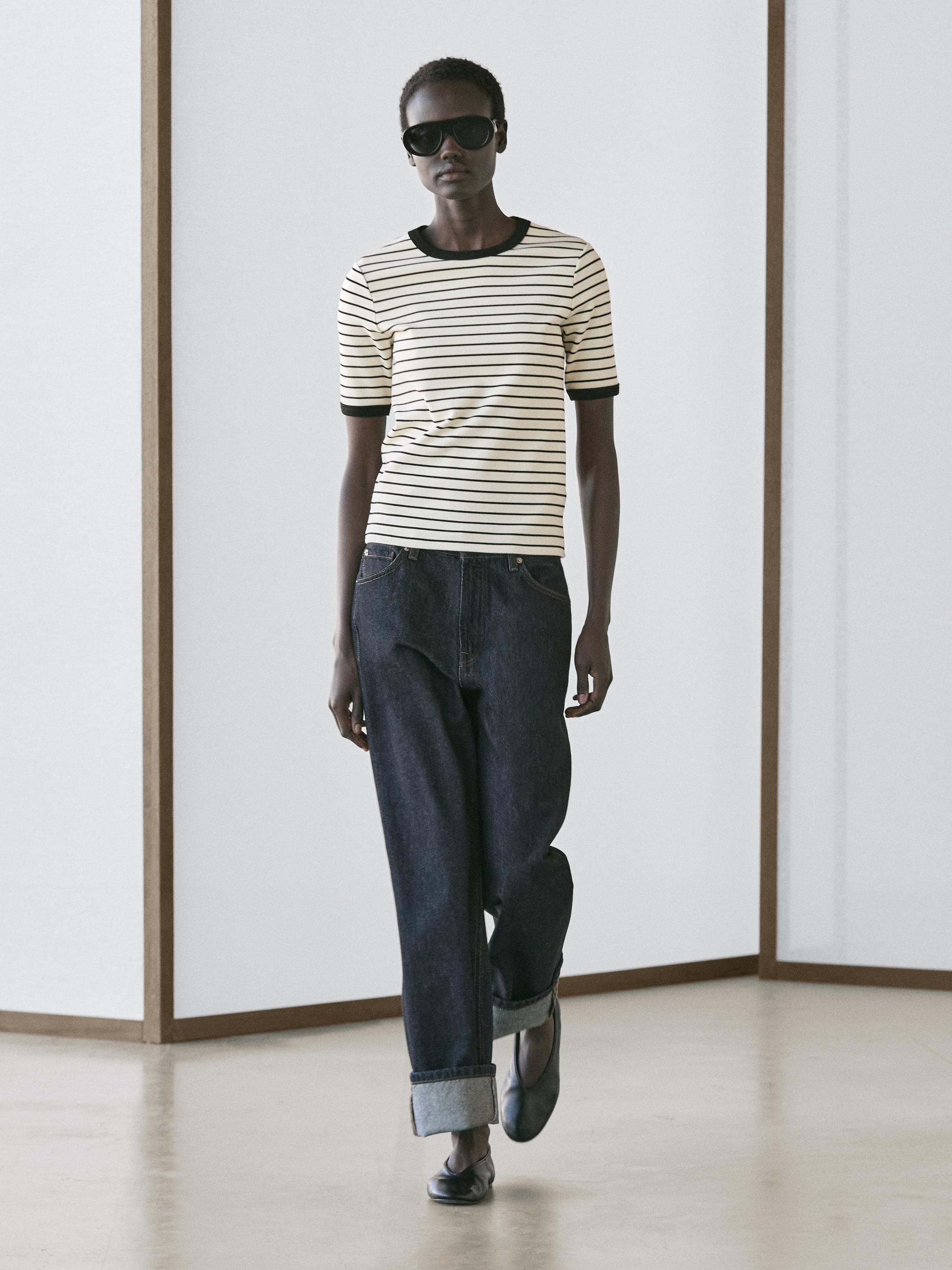 Set aus weißem T-Shirt mit schwarzen Streifen und dunklen Jeans mit umgeschlagenem Saum.