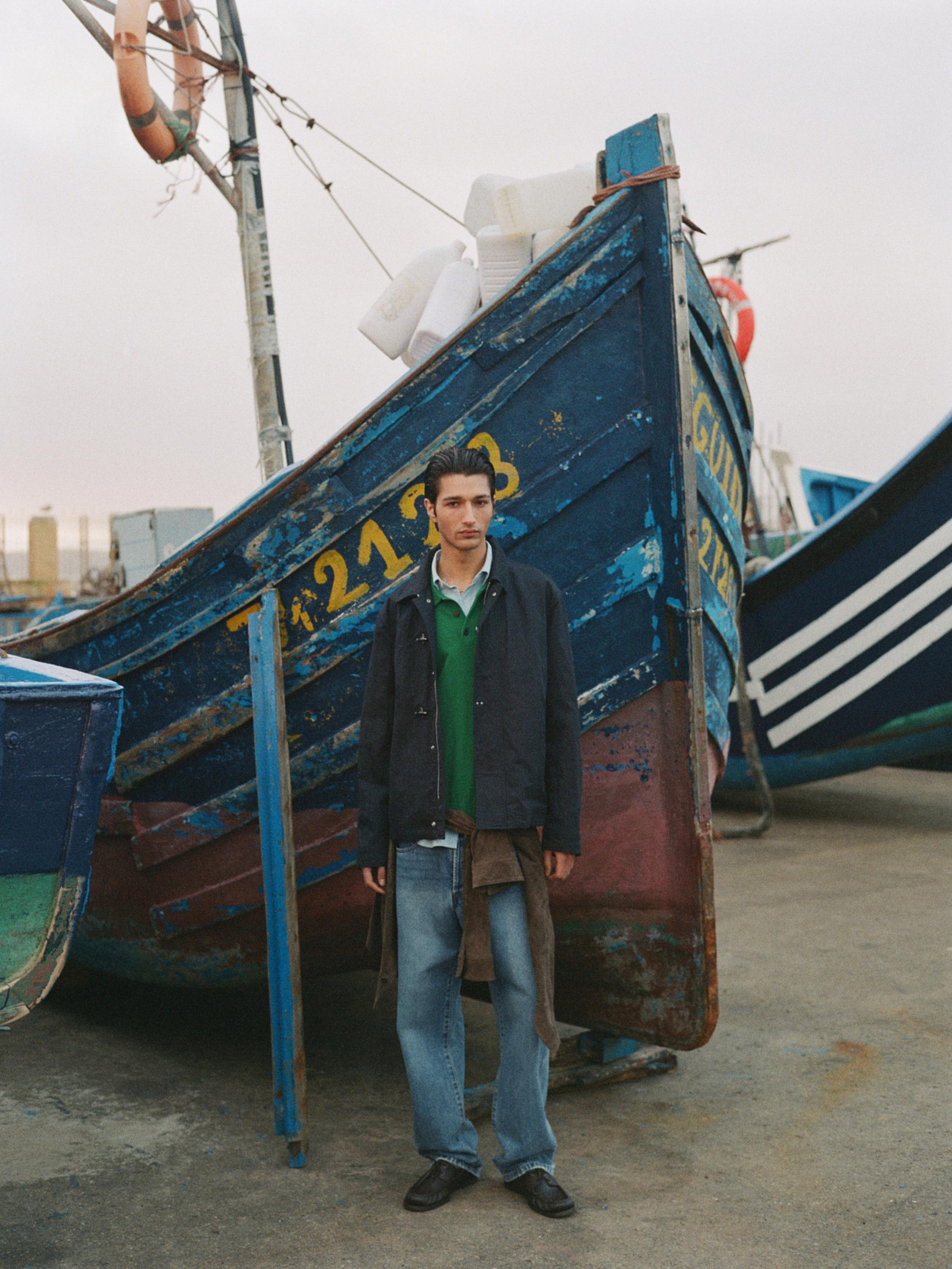 Ensemble composé d'une veste bleu marine, d'une chemise verte et d'un jean large.