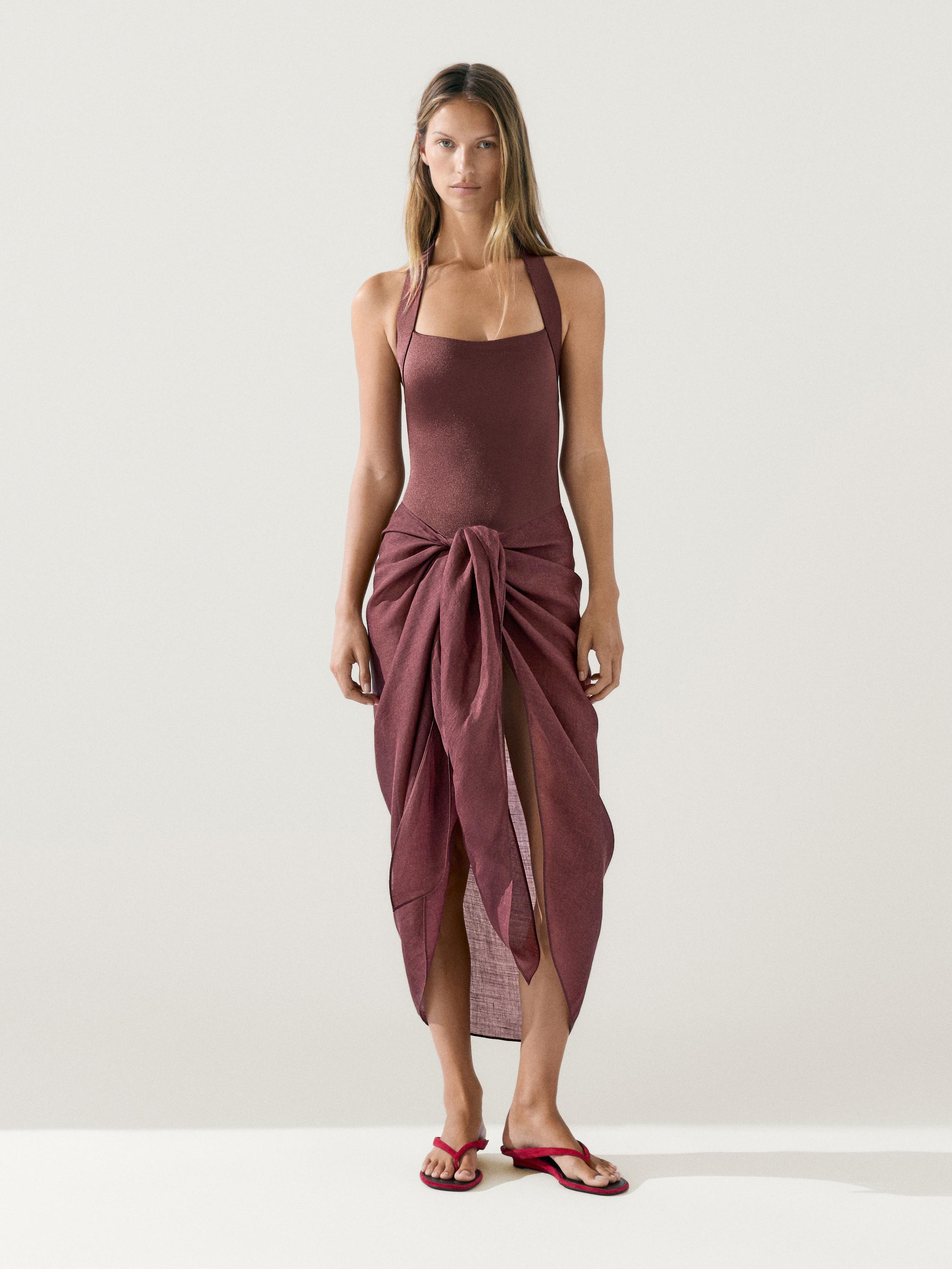 Conjunto de traje de baño café con falda pareo café anudada al frente y sandalias rojas.