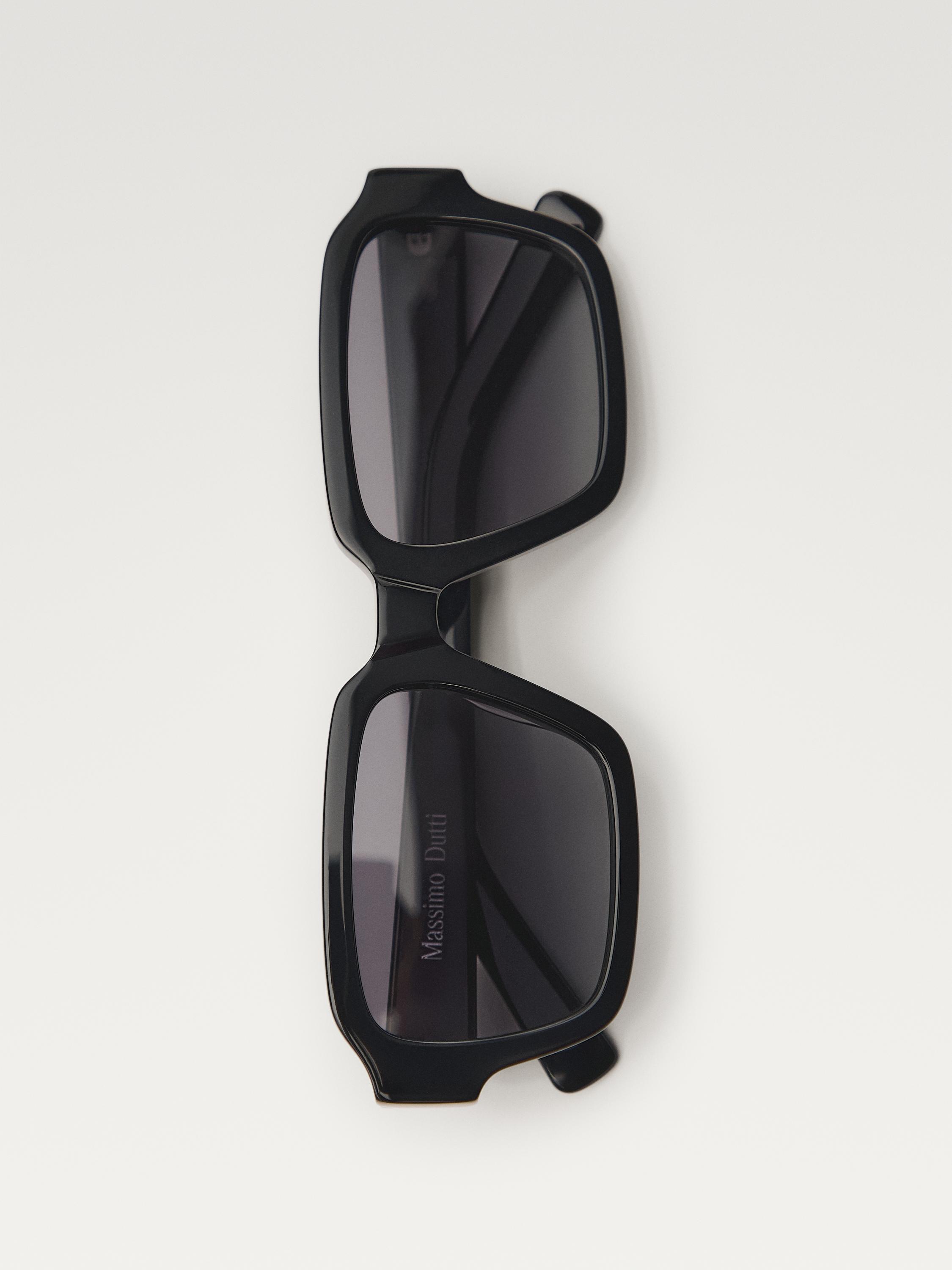 Kare çerçeveli ve koyu renkli camlara sahip siyah güneş gözlüğünün ön görünümü. Görünür metin: Sapında "Massimo Dutti".
