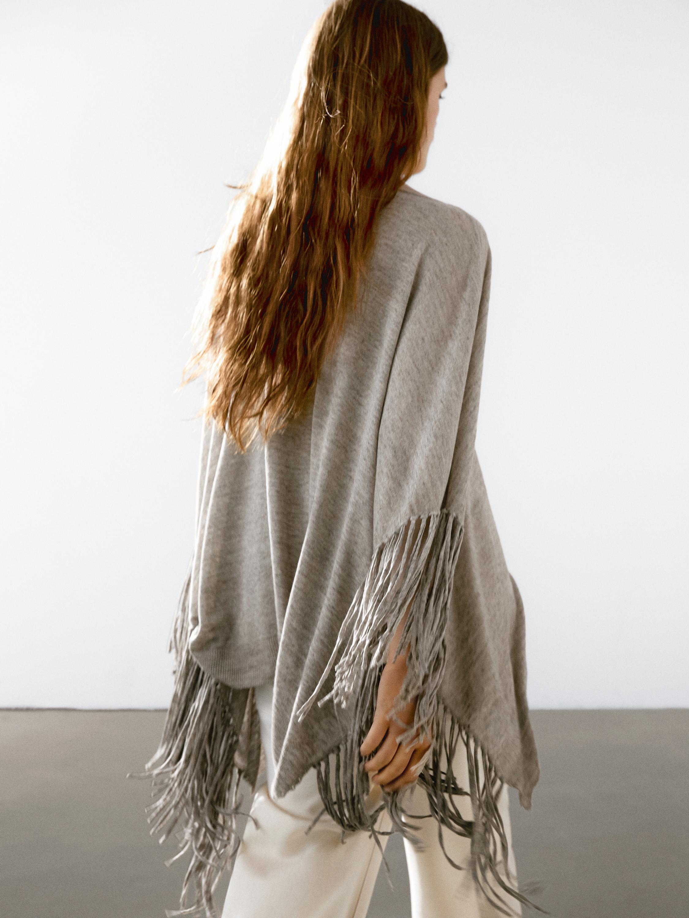 منظر خلفي لبونشو رمادي مع شراشيب طويلة على الأكمام والحافة السفلية.