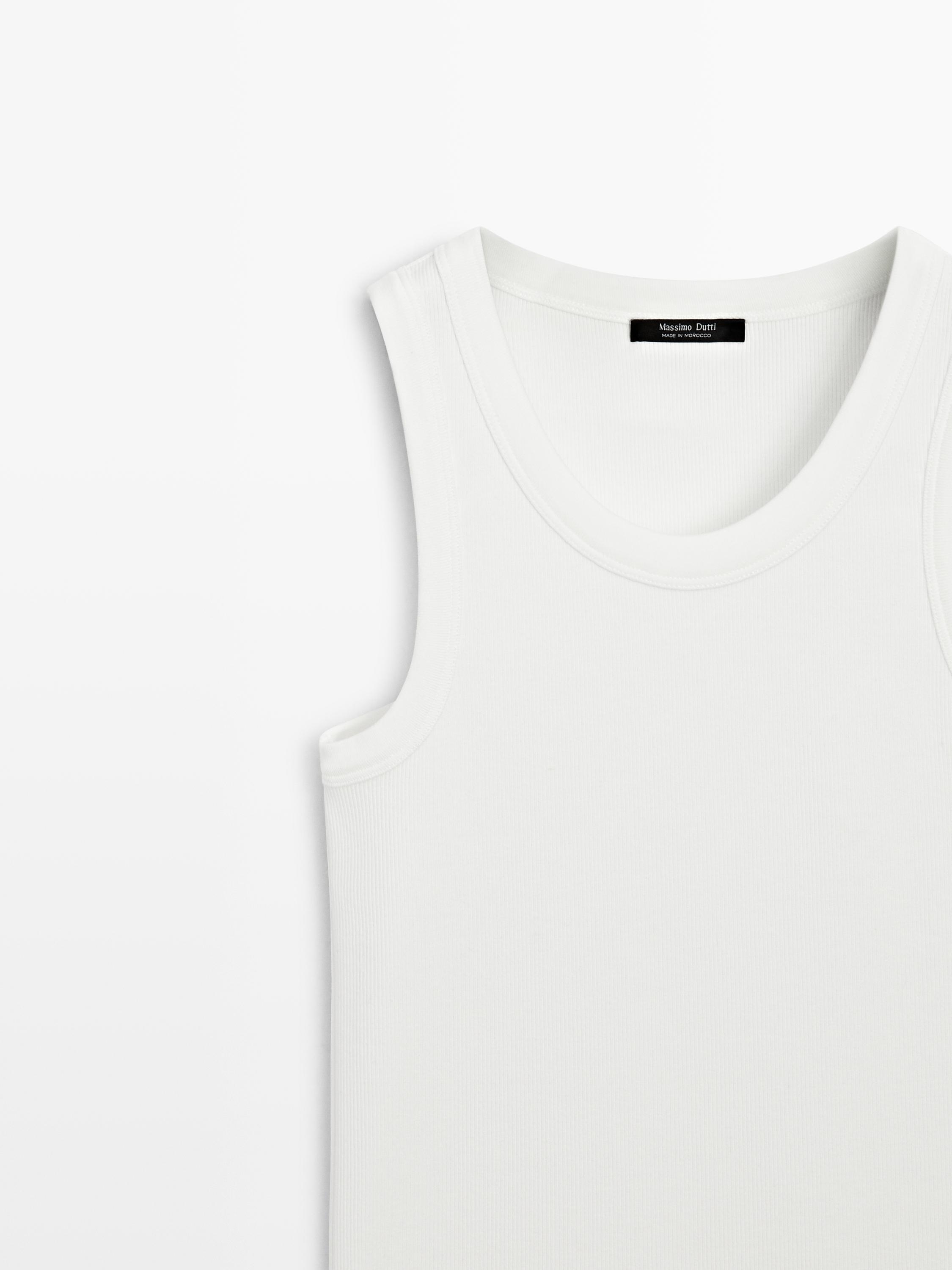 "Detail of white sleeveless top with round neck."