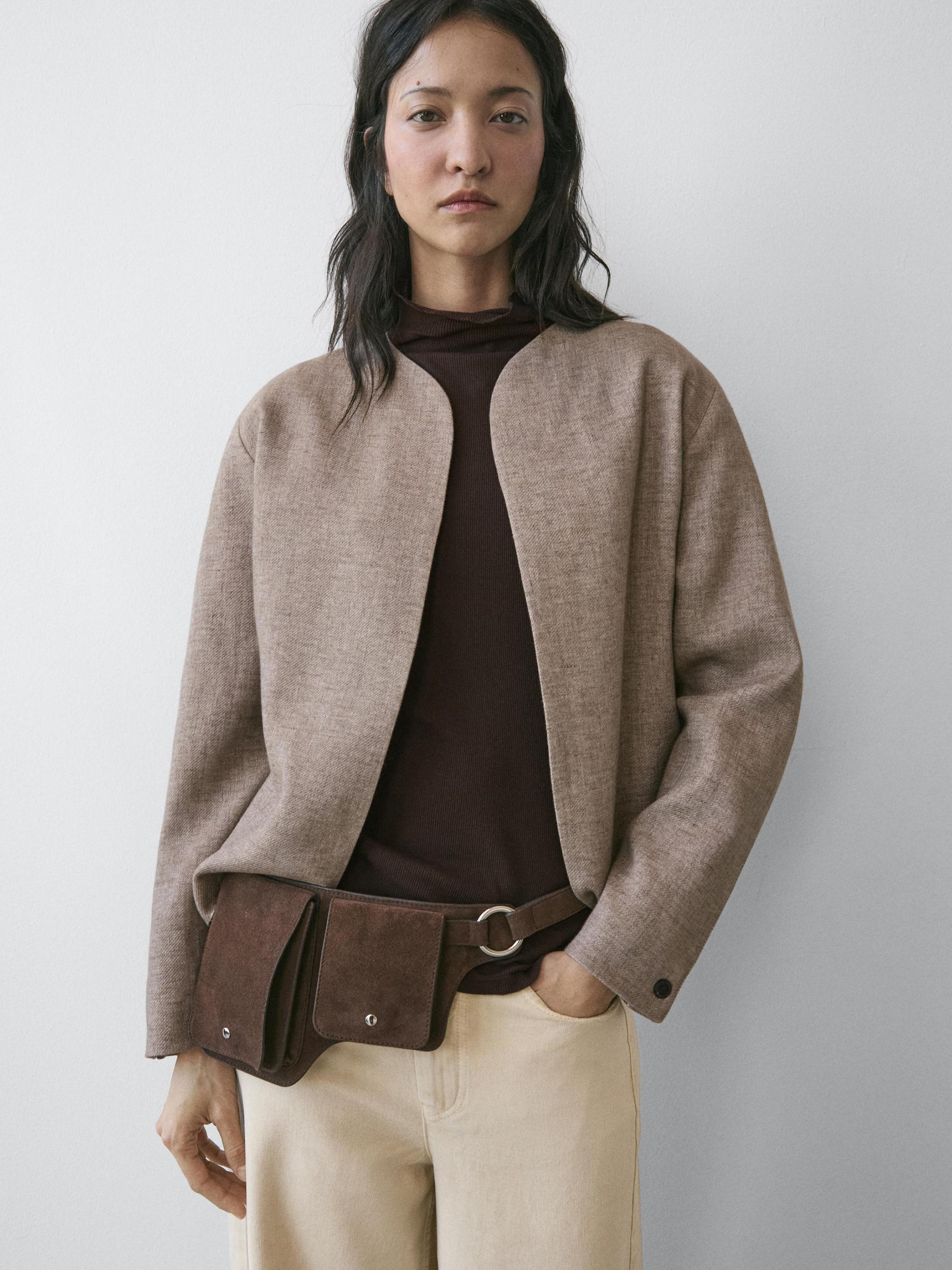 Bộ blazer màu nâu xám nhạt dáng crop, áo thun màu nâu sẫm và quần tây màu be. Túi đeo hông màu nâu với khóa cài nút nổi bật.