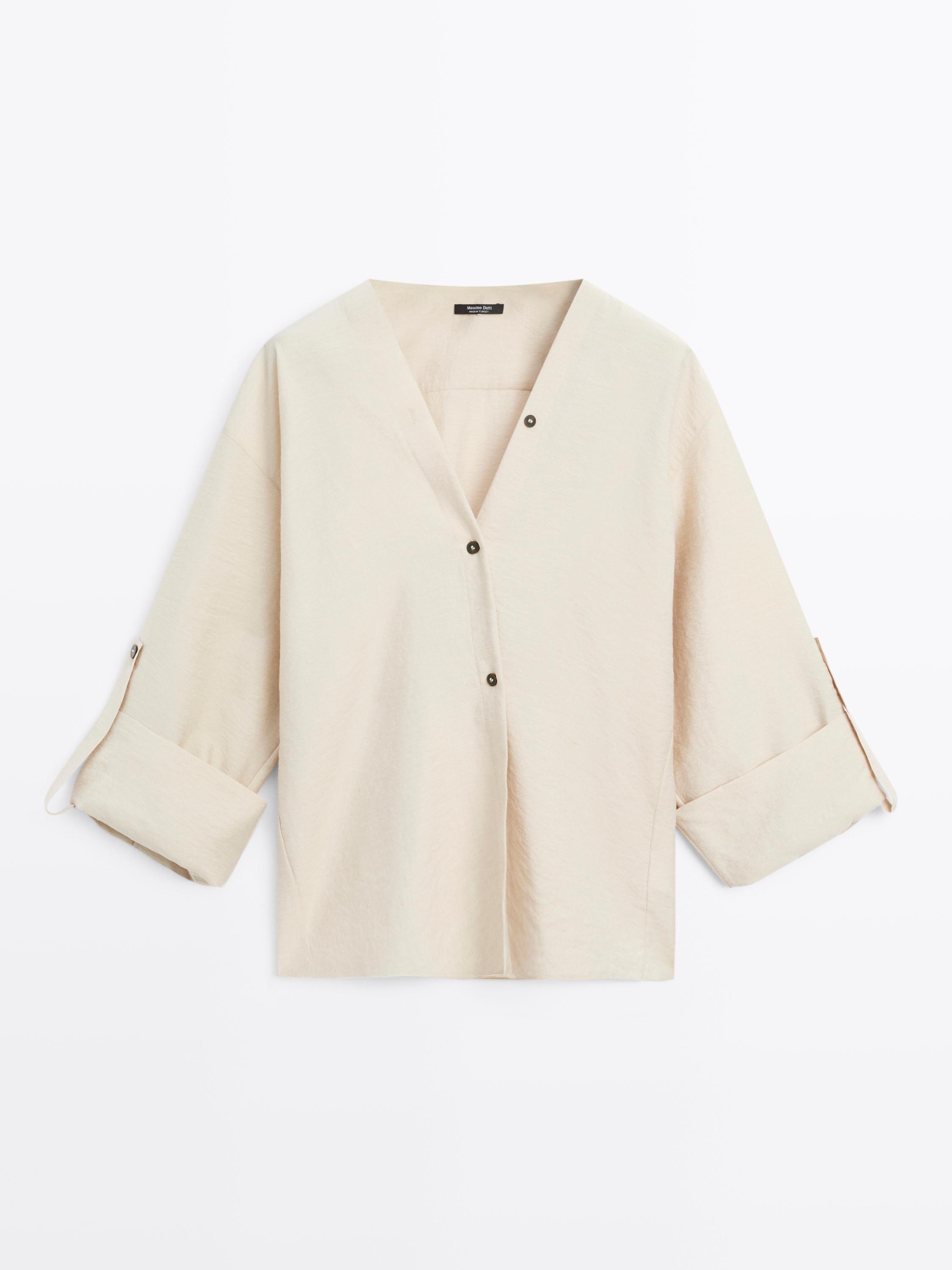 Sprednji pogled na srajco barve ecru z V-izrezom, dolgimi rokavi z možnostjo zavihanja in zapenjanjem s temnimi gumbi.