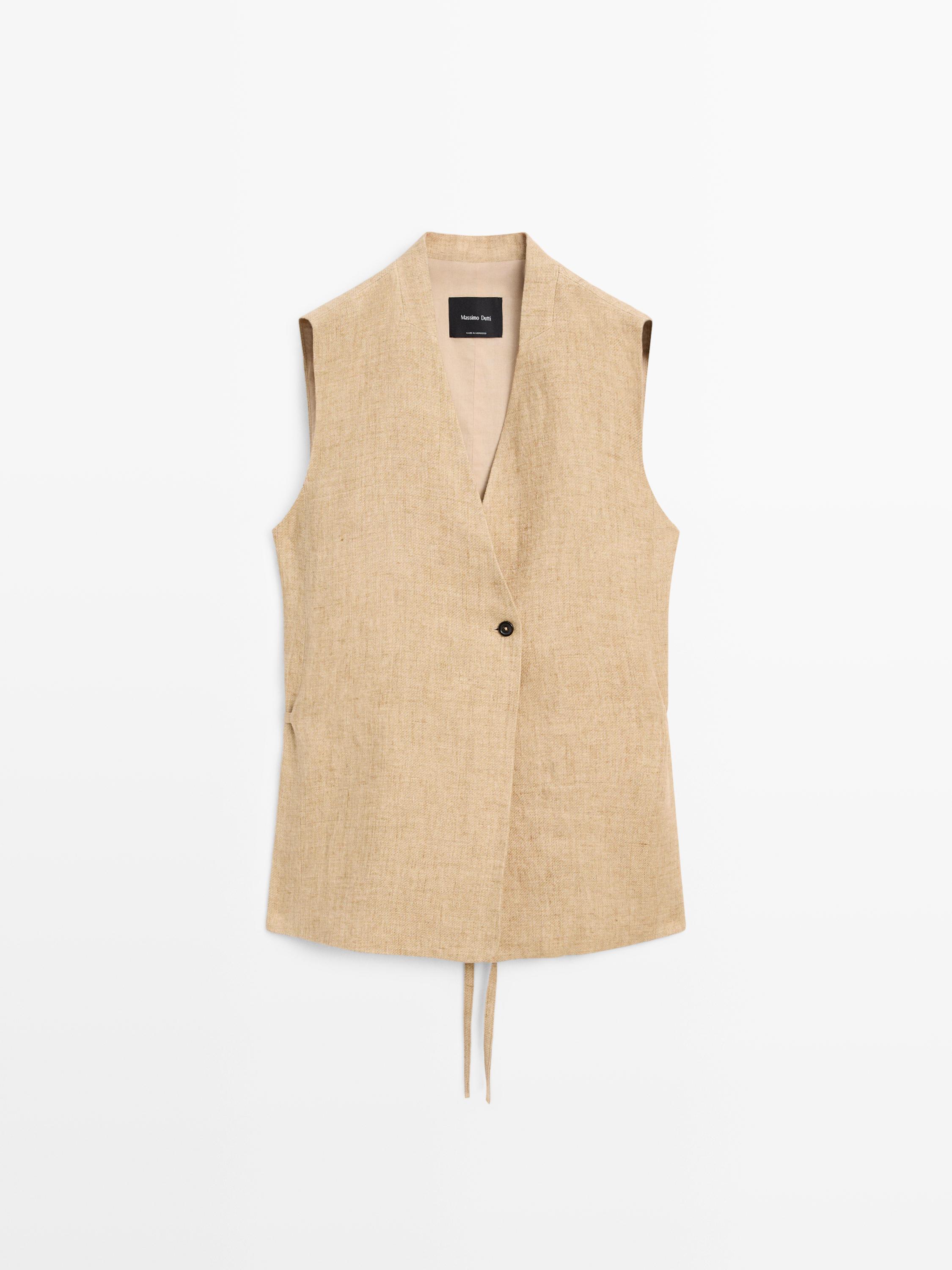 Vista frontal de chaleco beige con cierre cruzado y un botón visible.