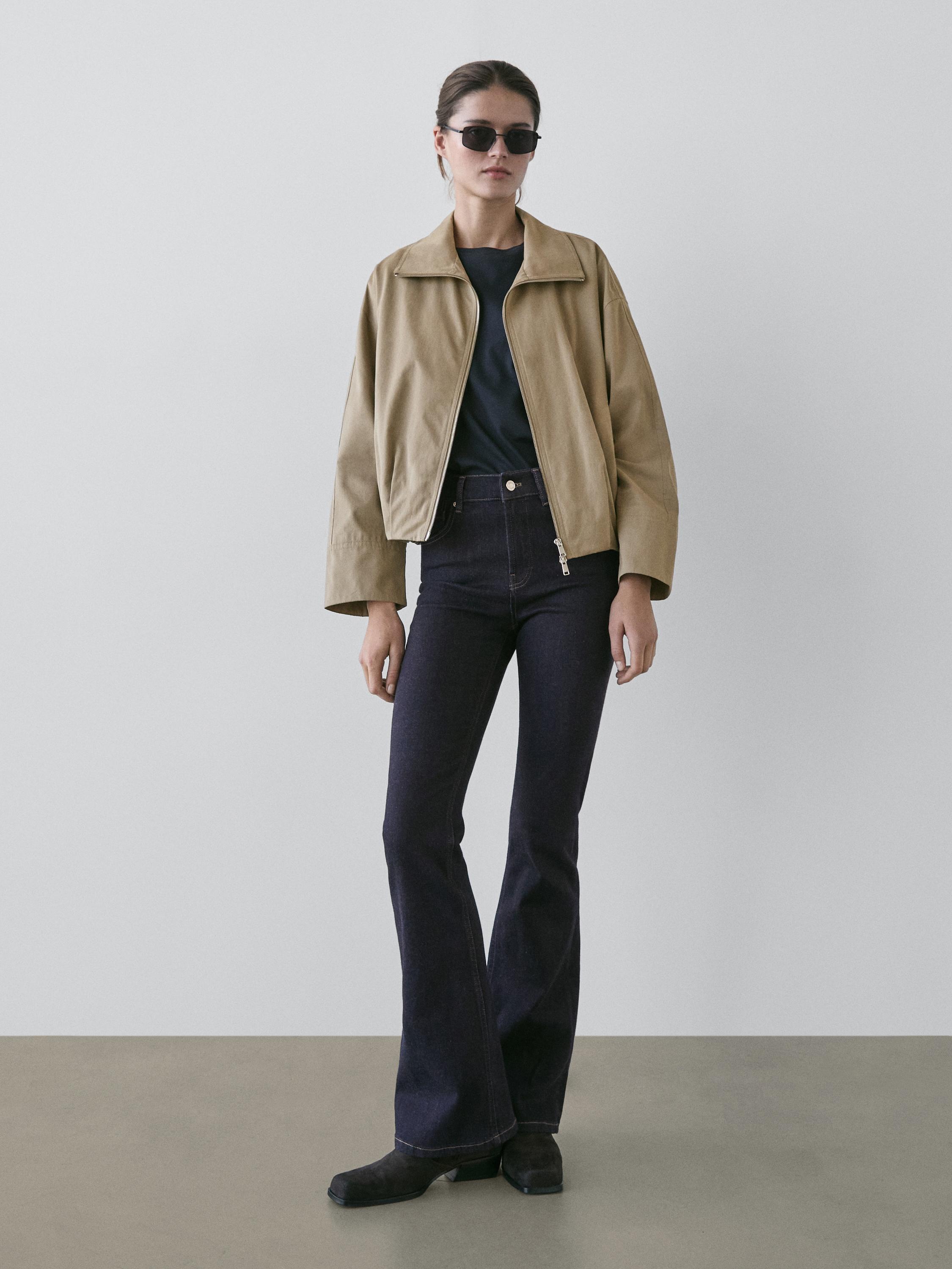 Ensemble veste zippée beige et jean flare bleu foncé.