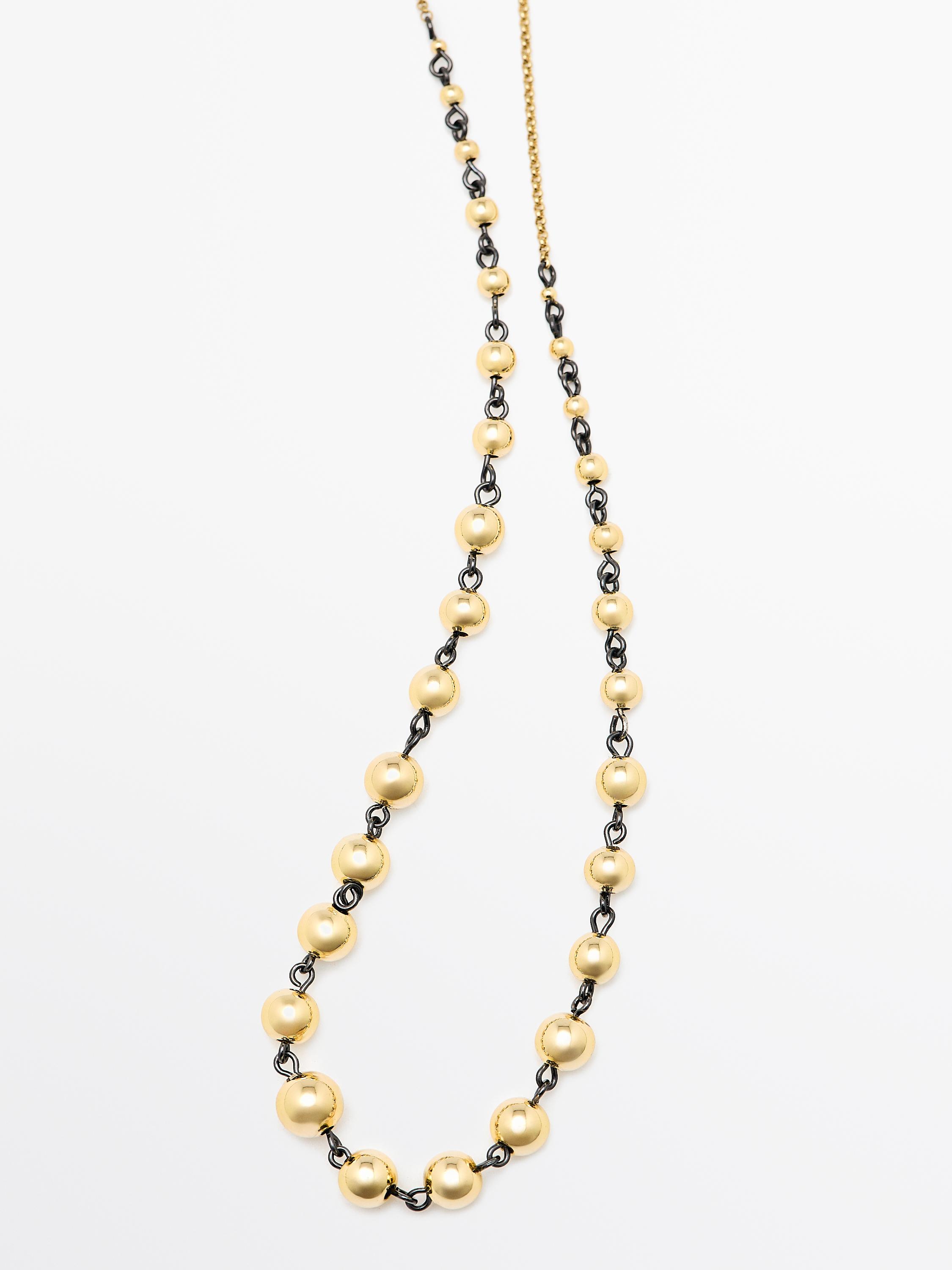 Colar dourado con contas redondas e cadea negra.