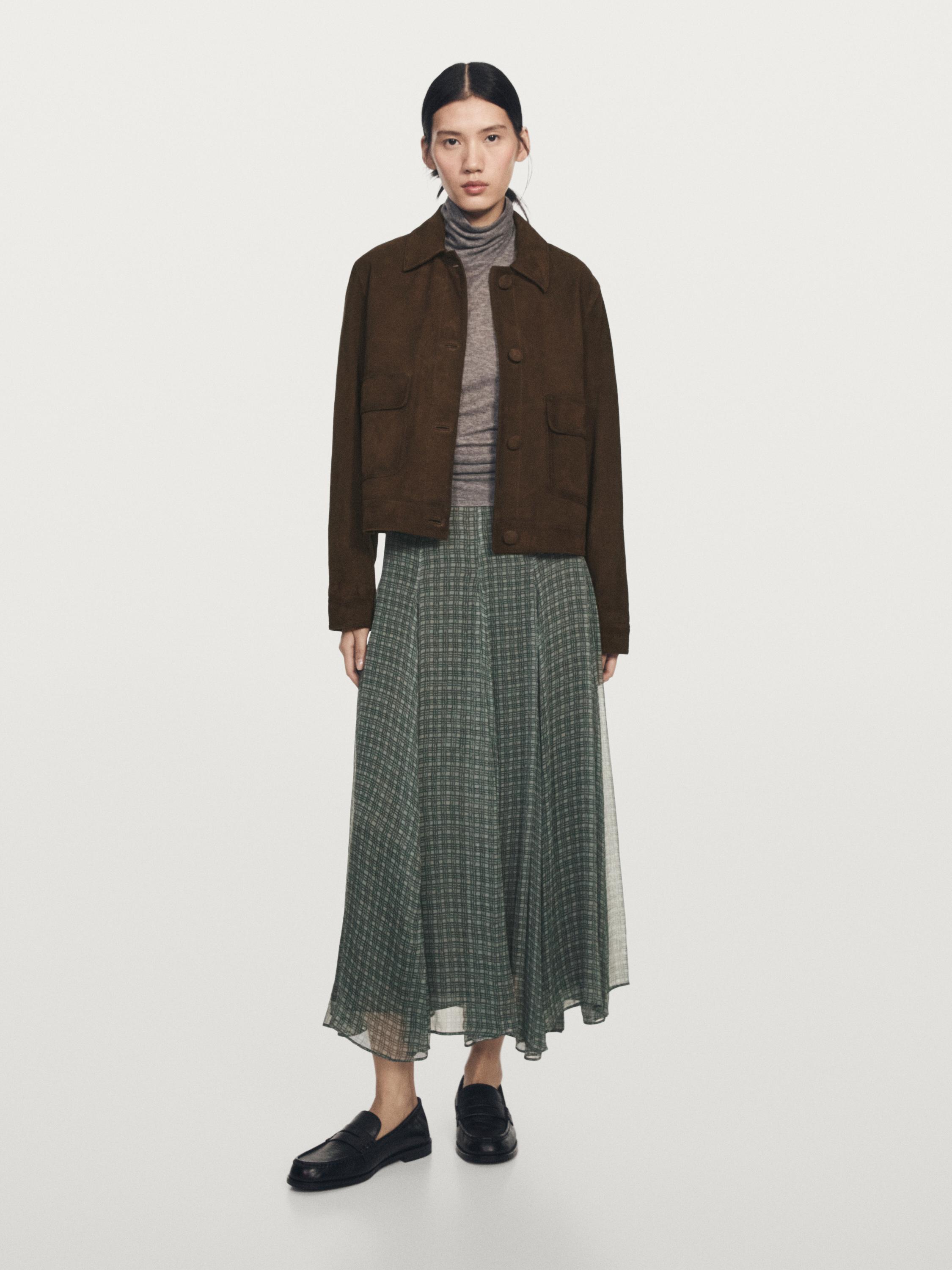 Conjunto de chaqueta marrón con bolsillos, jersey gris de cuello alto y falda midi verde estampada.