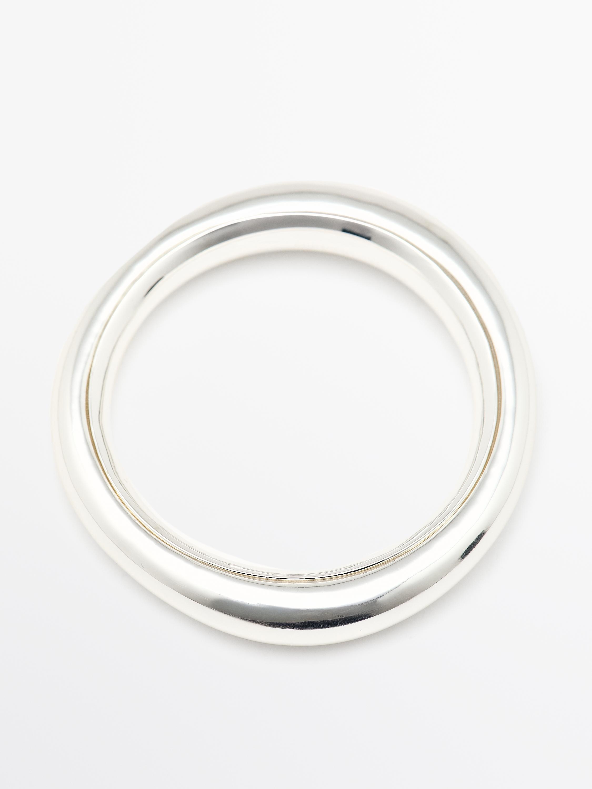 Vooraanzicht van een zilverkleurige stijve armband met een circulair ontwerp en een glanzende afwerking.