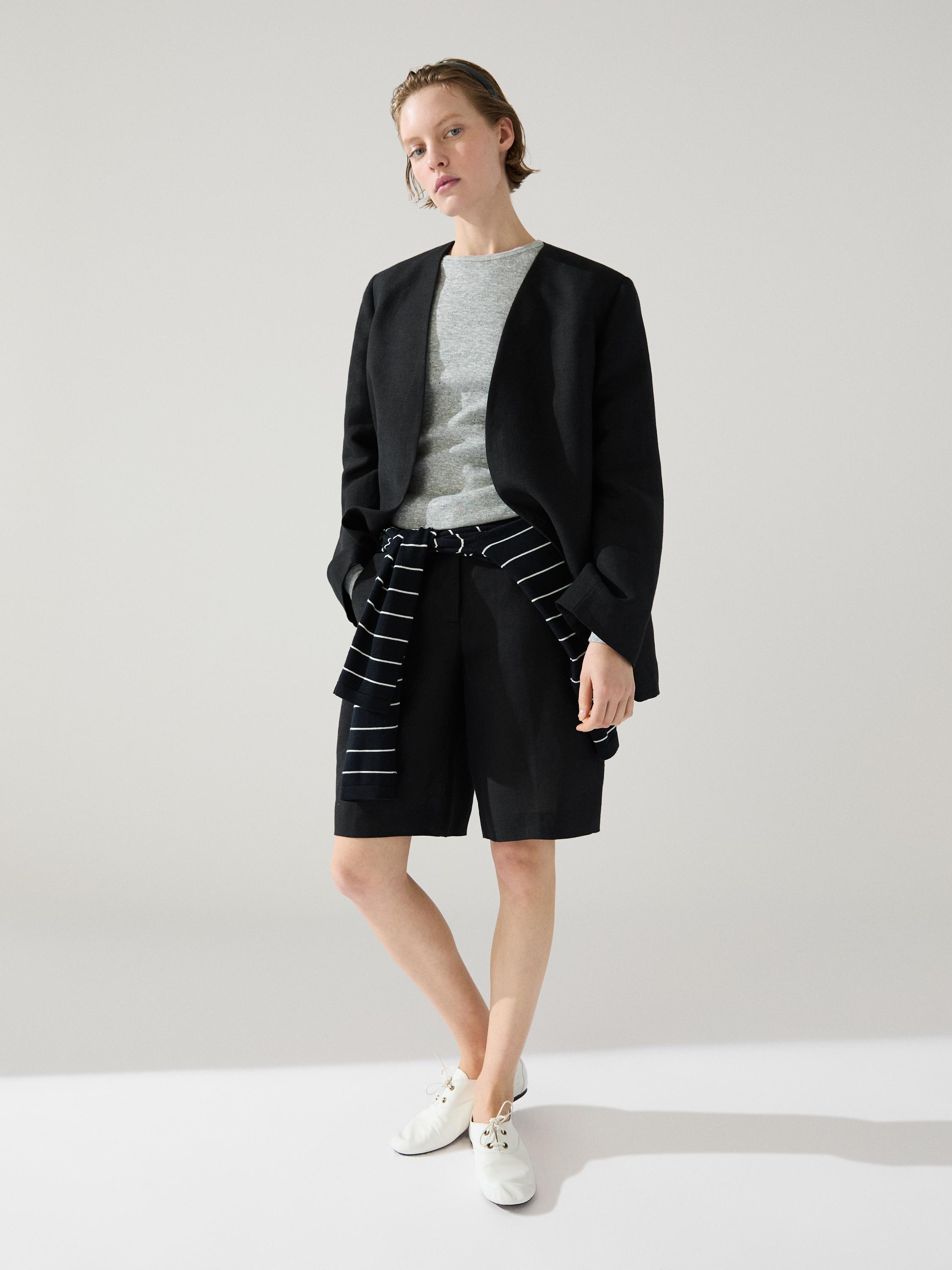 Conjunto de blazer negro, camiseta gris, bermudas negras, suéter a rayas atado a la cintura y zapatos blancos.