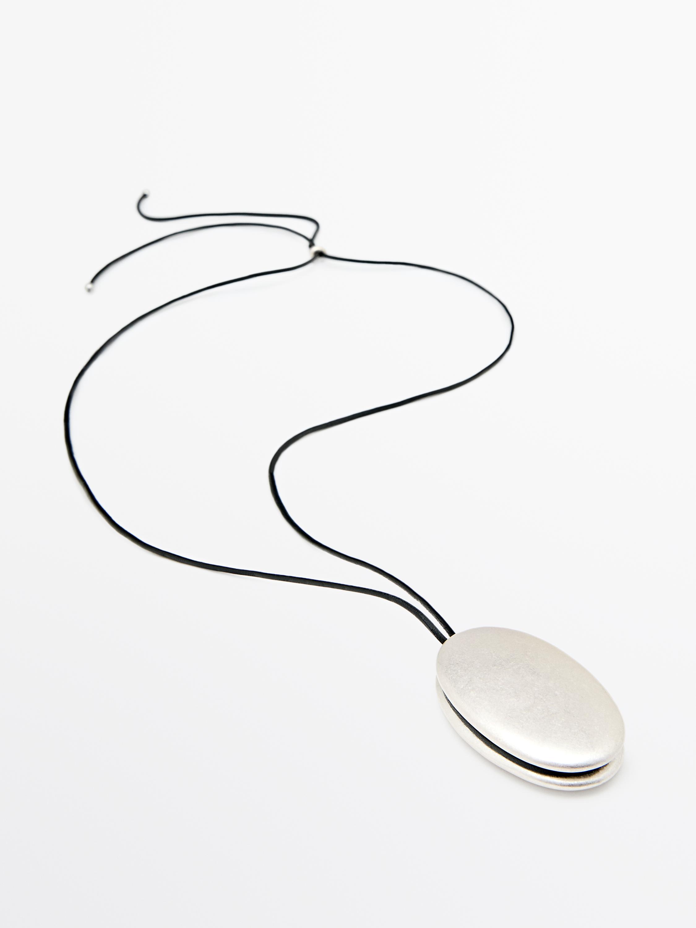 Necklace with an oval silver-colored metal piece and a black cord.