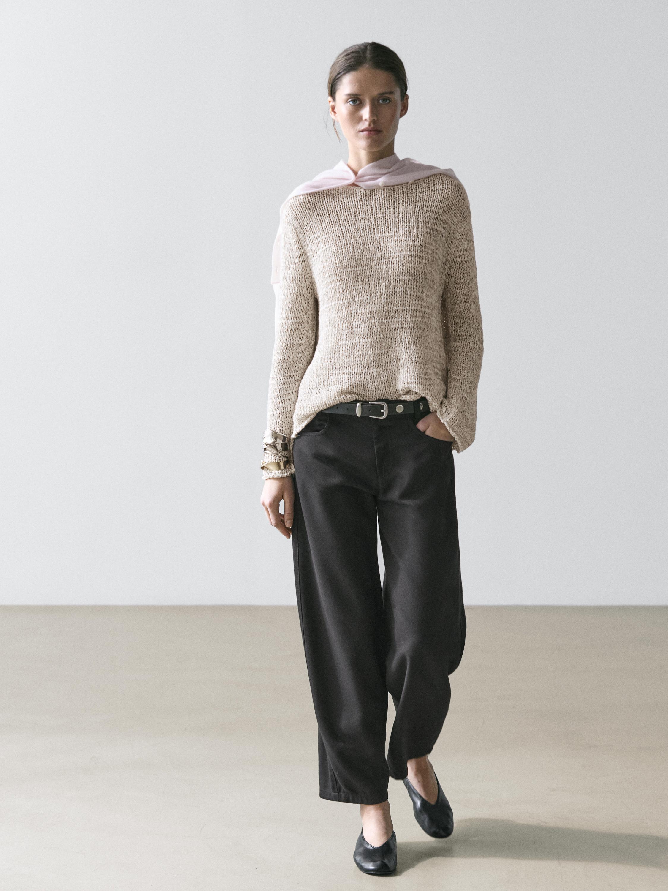 Completo di maglione beige a maglia e pantaloni neri a taglio ampio con cintura e scarpe nere.