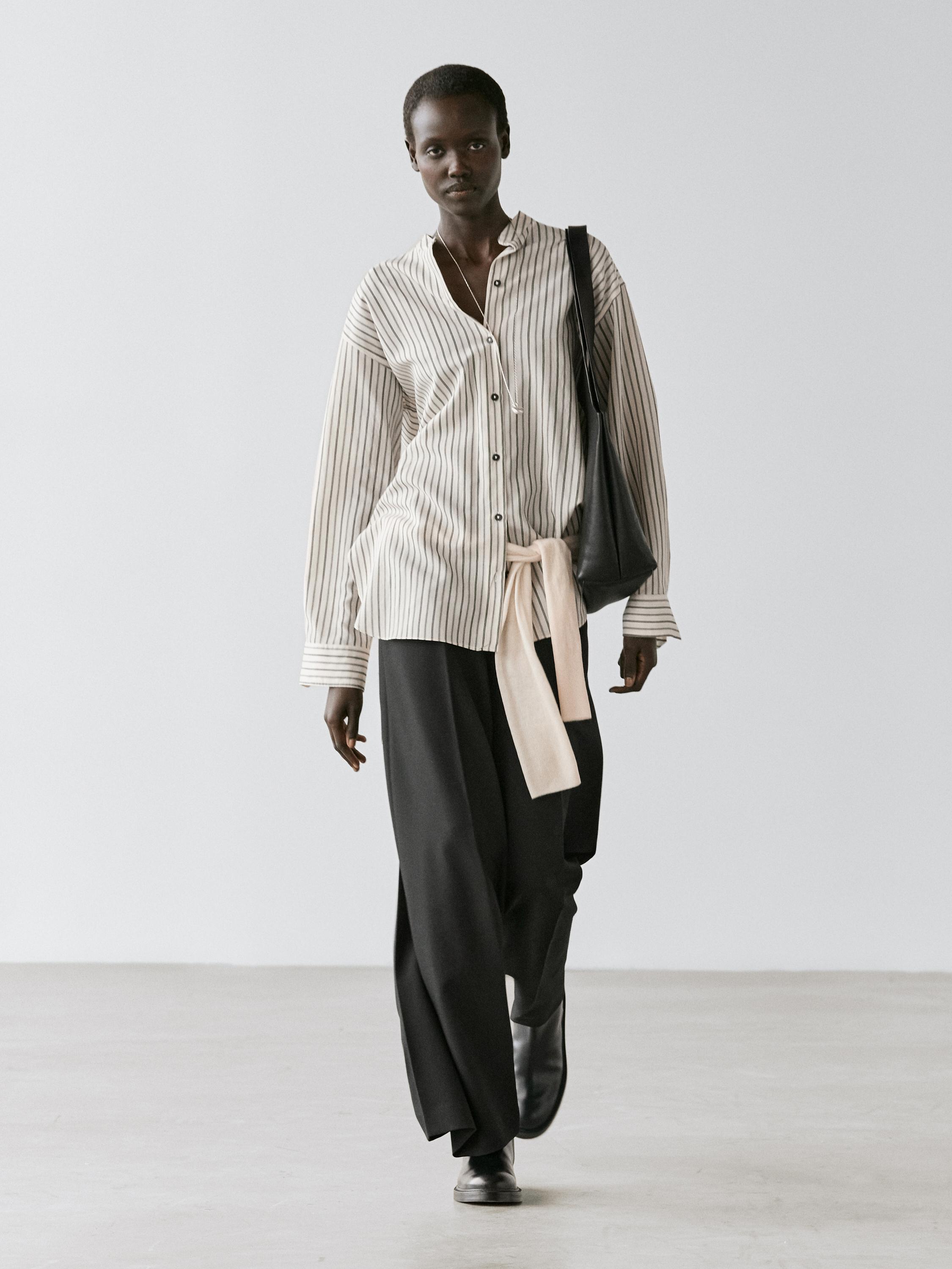 Conjunto de camisa blanca con rayas y cuello mao, pantalones negros anchos y botas negras.