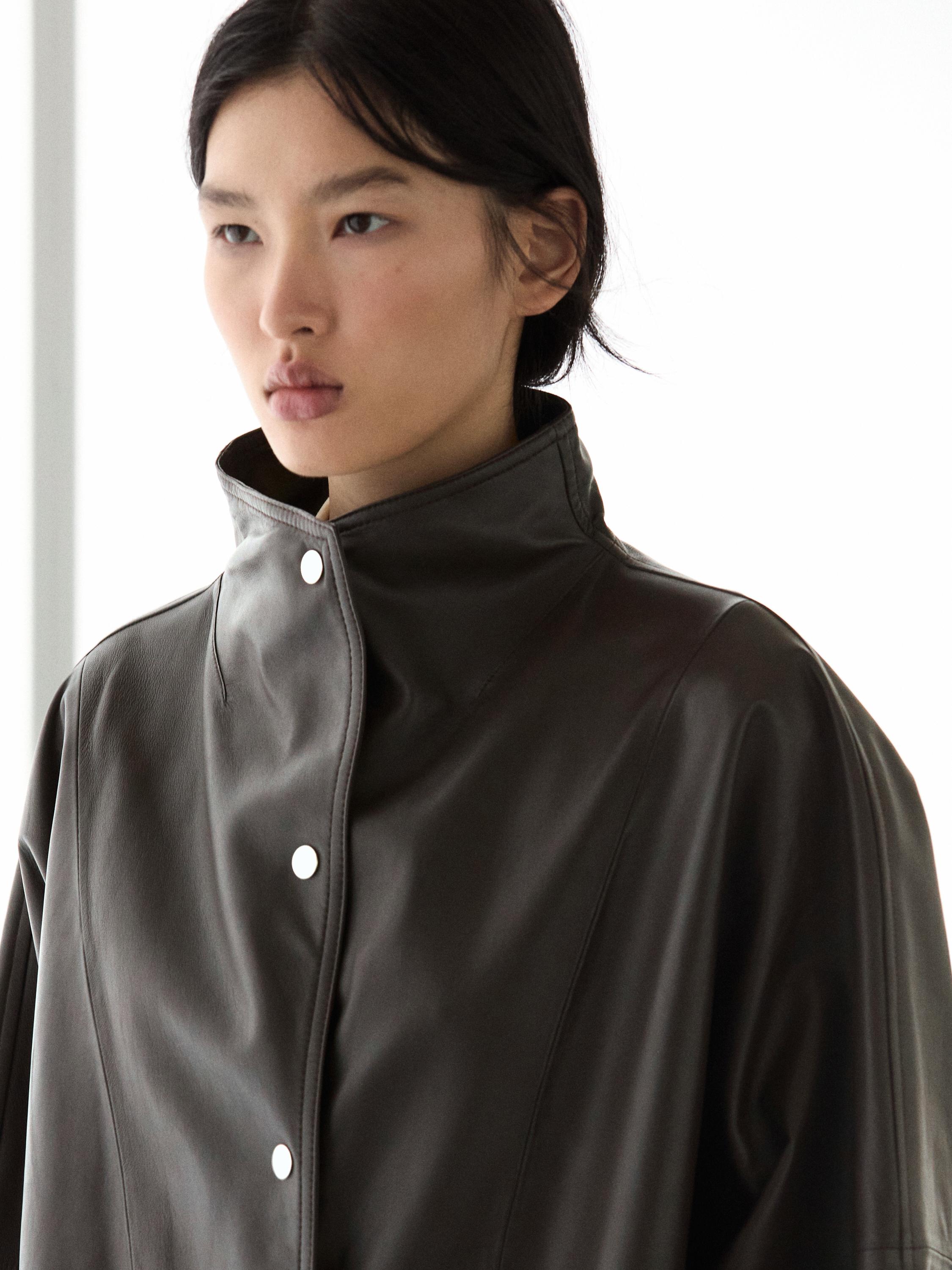 Halflang shot van een bruine jas met een hoge kraag en zichtbare knopen aan de voorkant.