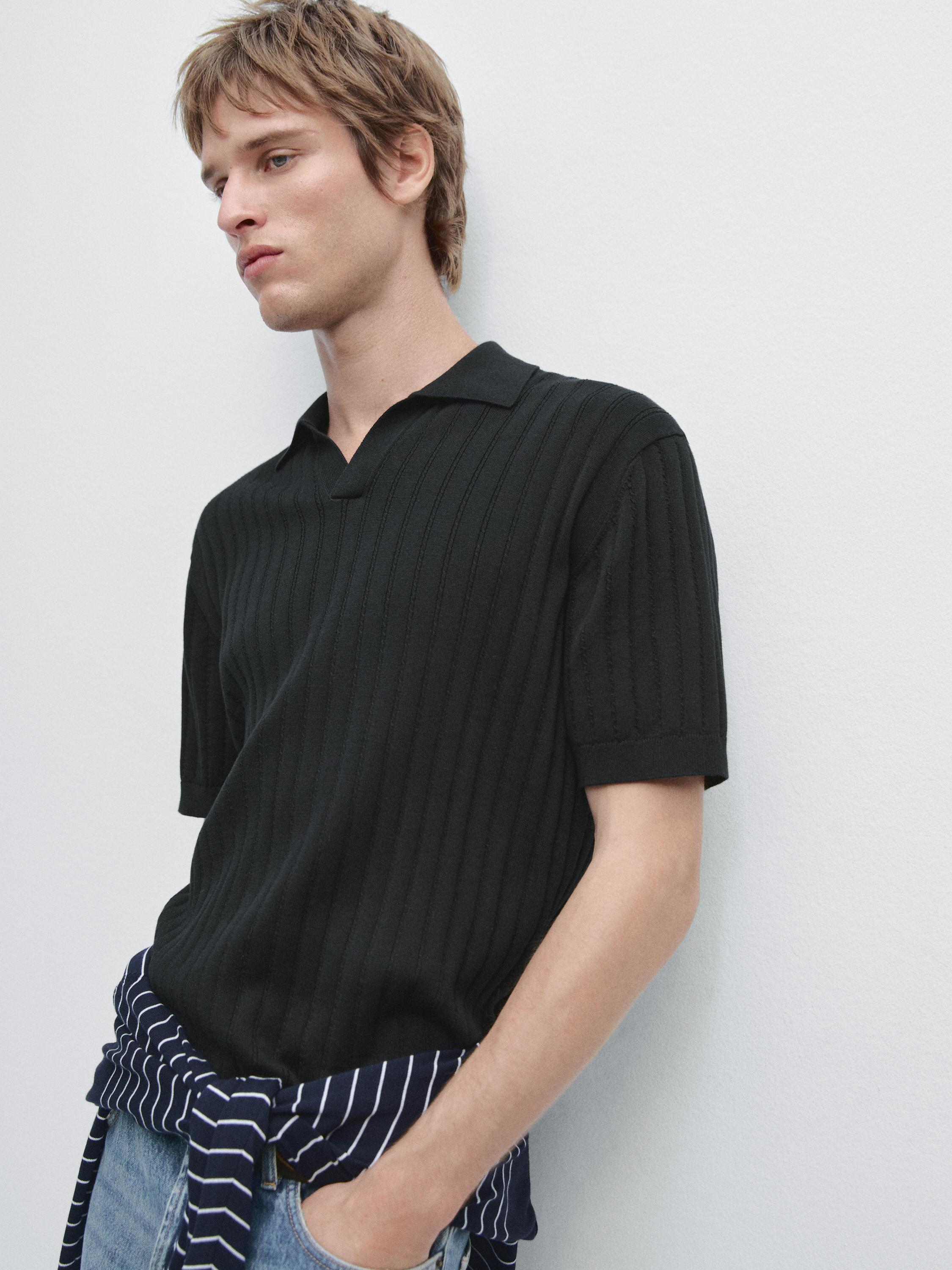 Plano medio de xersei polo azul mariño con punto trenzado e mangas curtas. Camisa de raias atada á cintura.