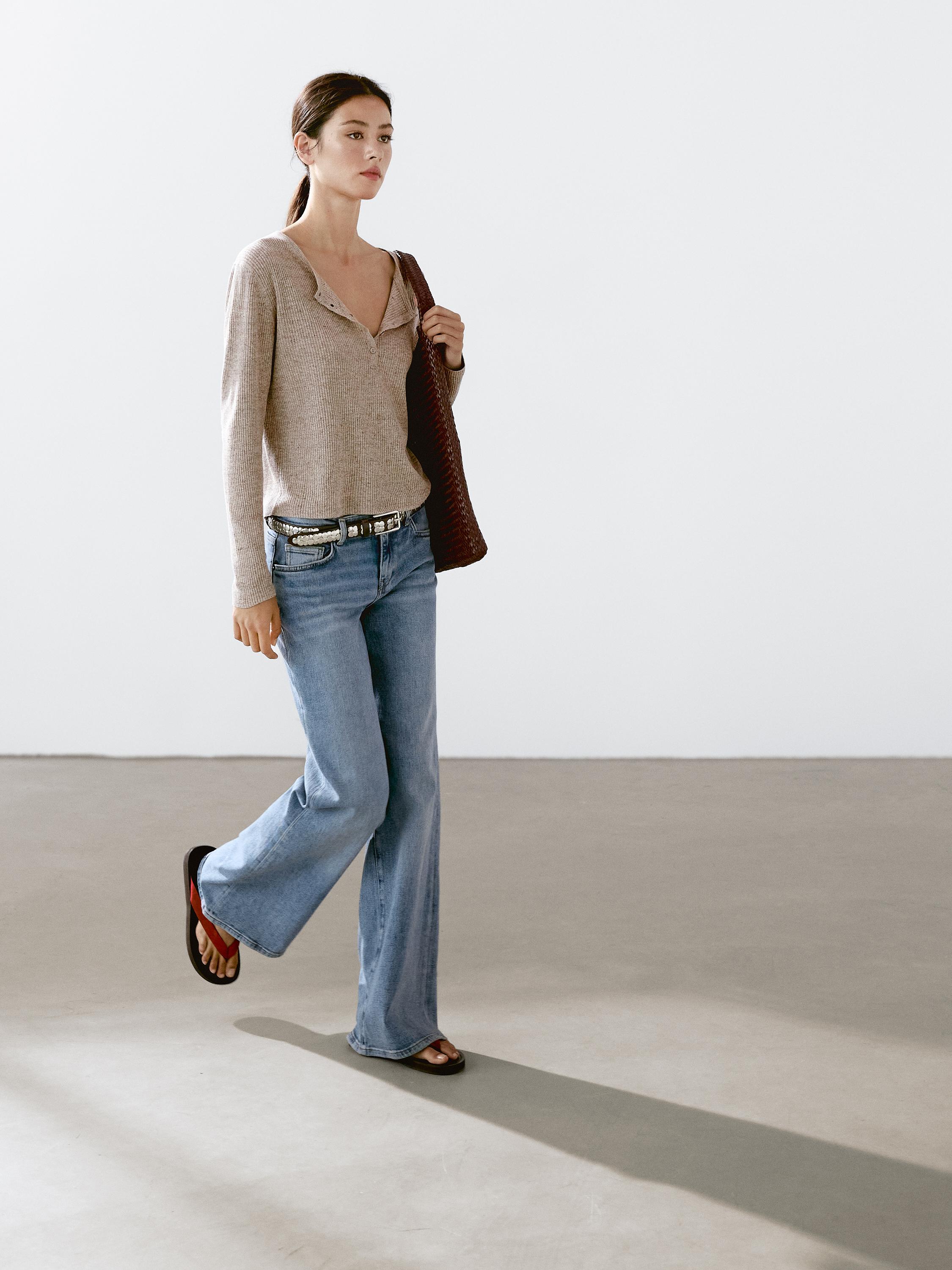 طقم كنزة بيج بياقة مفتوحة وجينز أزرق واسع مع صندل.