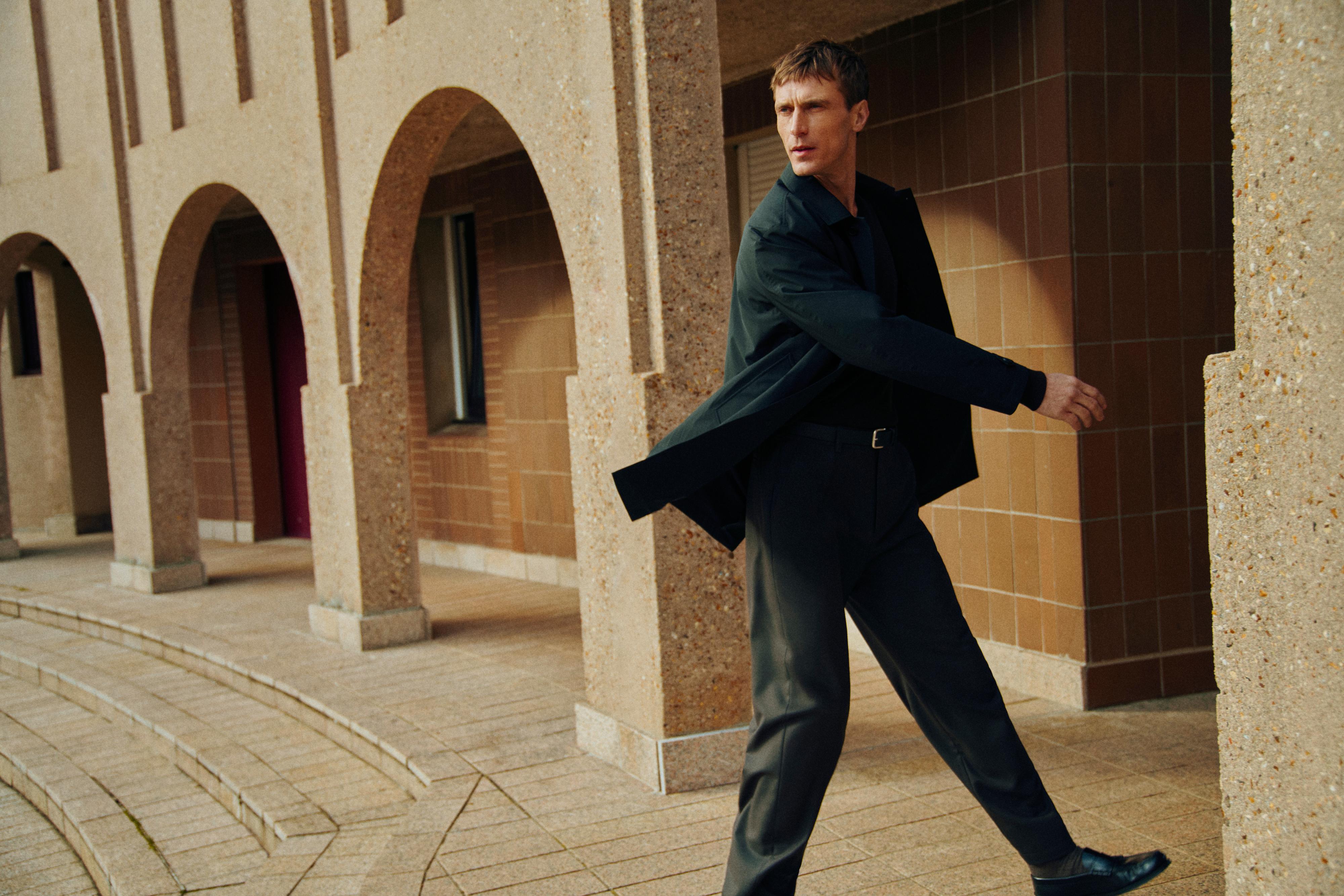 Conjunto de chaqueta negra y pantalón gris oscuro, con cinturón negro visible.