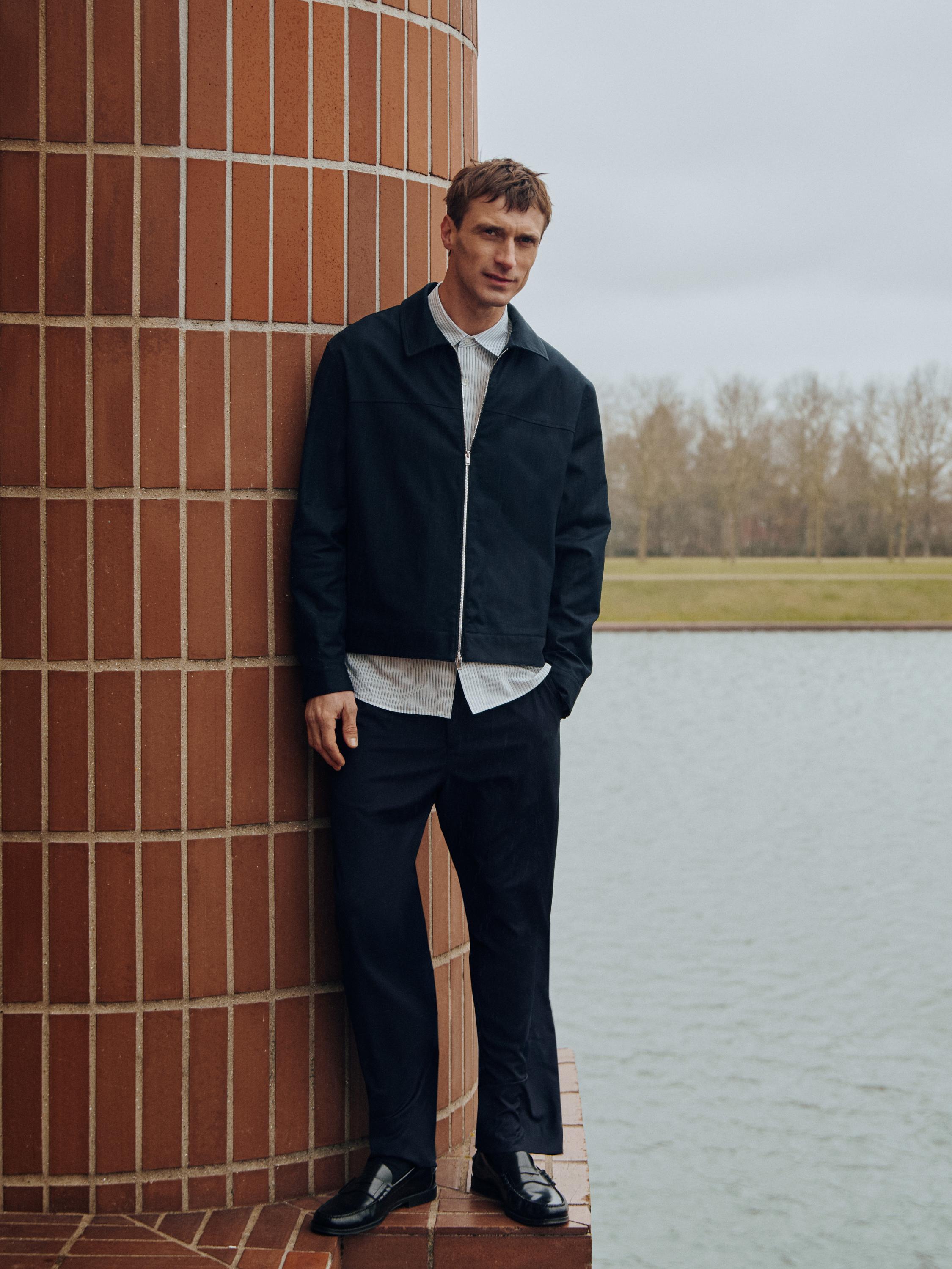 Комплект, состоящий из темно-синей куртки на молнии, белой рубашки в полоску и темно-синих брюк.