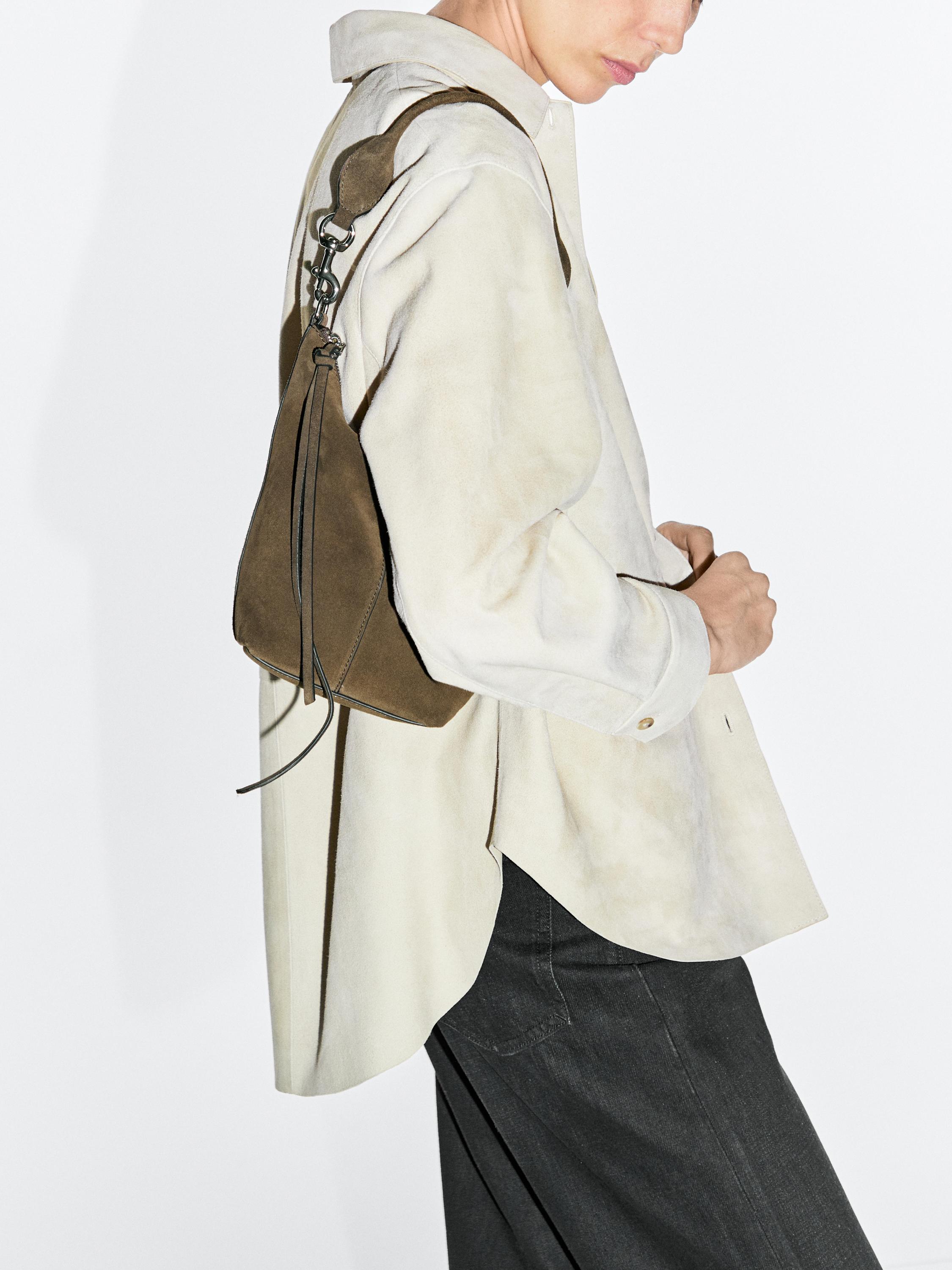 Medium shot of a khaki purse with an adjustable strap and zipper closure, paired with a white shirt and dark pants.